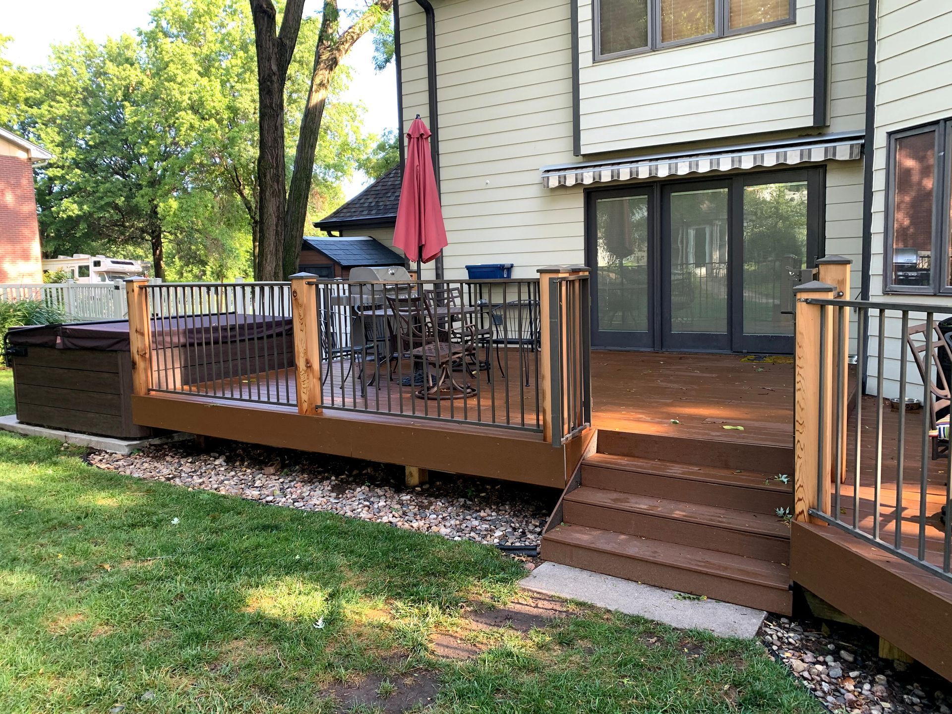 A large wooden deck with stairs and a red umbrella in front of a house.
