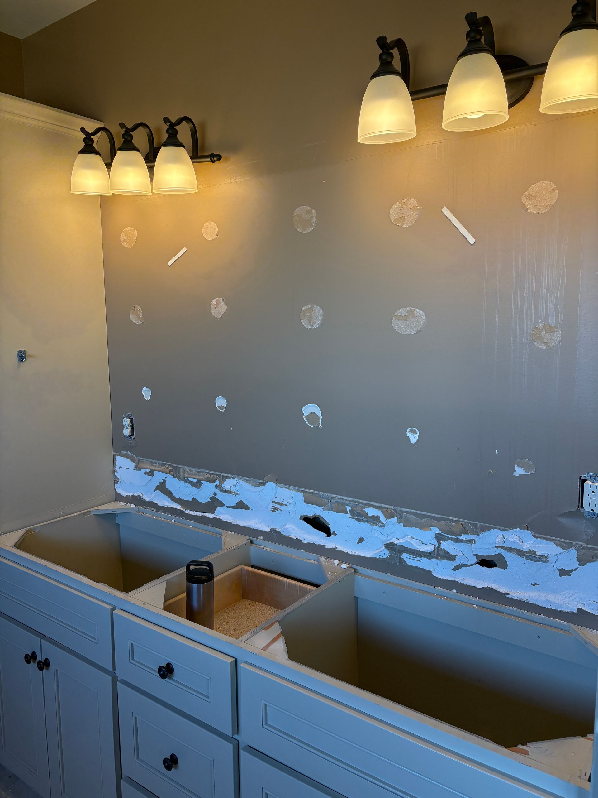 Bathroom with vanity, lighting fixture, and wall with patched holes. Beige and white tones.