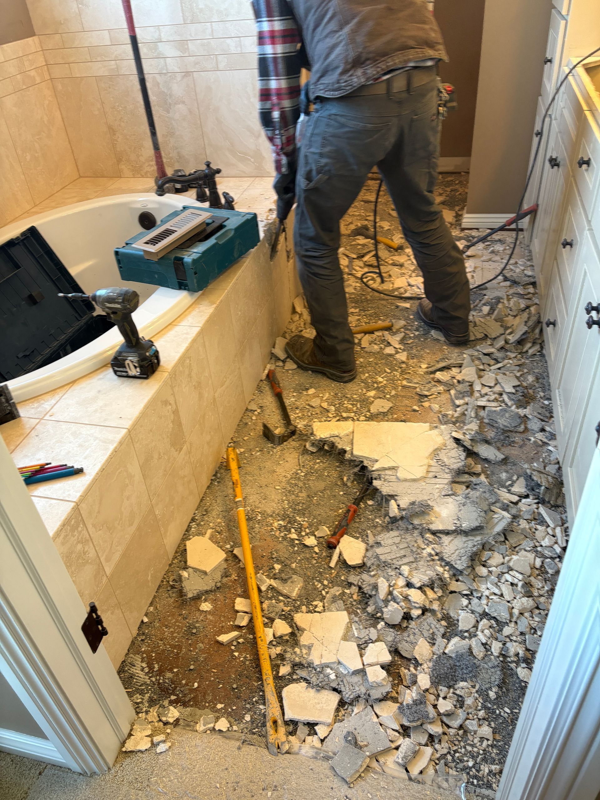 A person demolishes tile flooring in a bathroom with a hammer and other tools.
