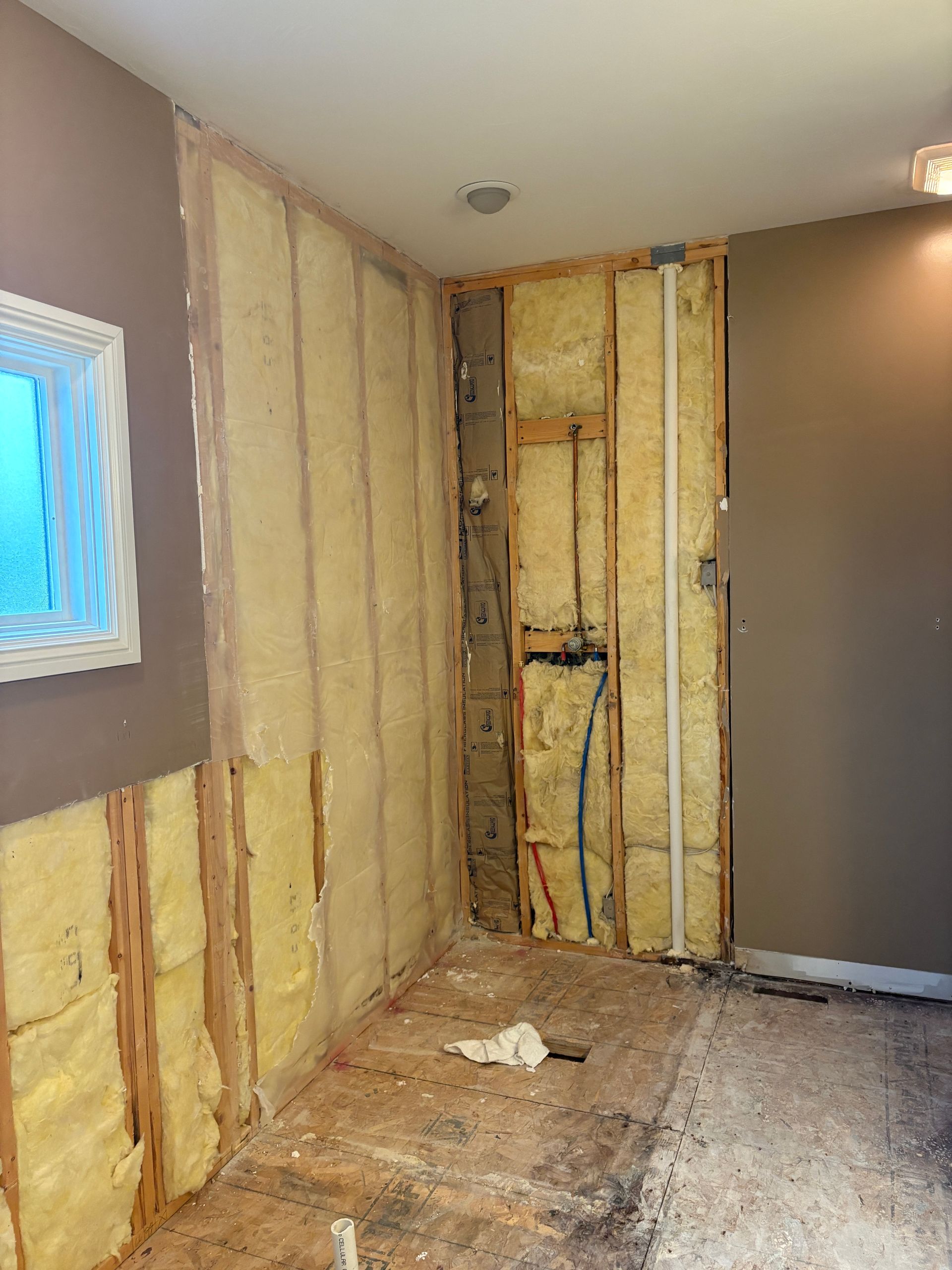 Bathroom renovation: walls stripped to studs, insulation visible. Plumbing and window present.
