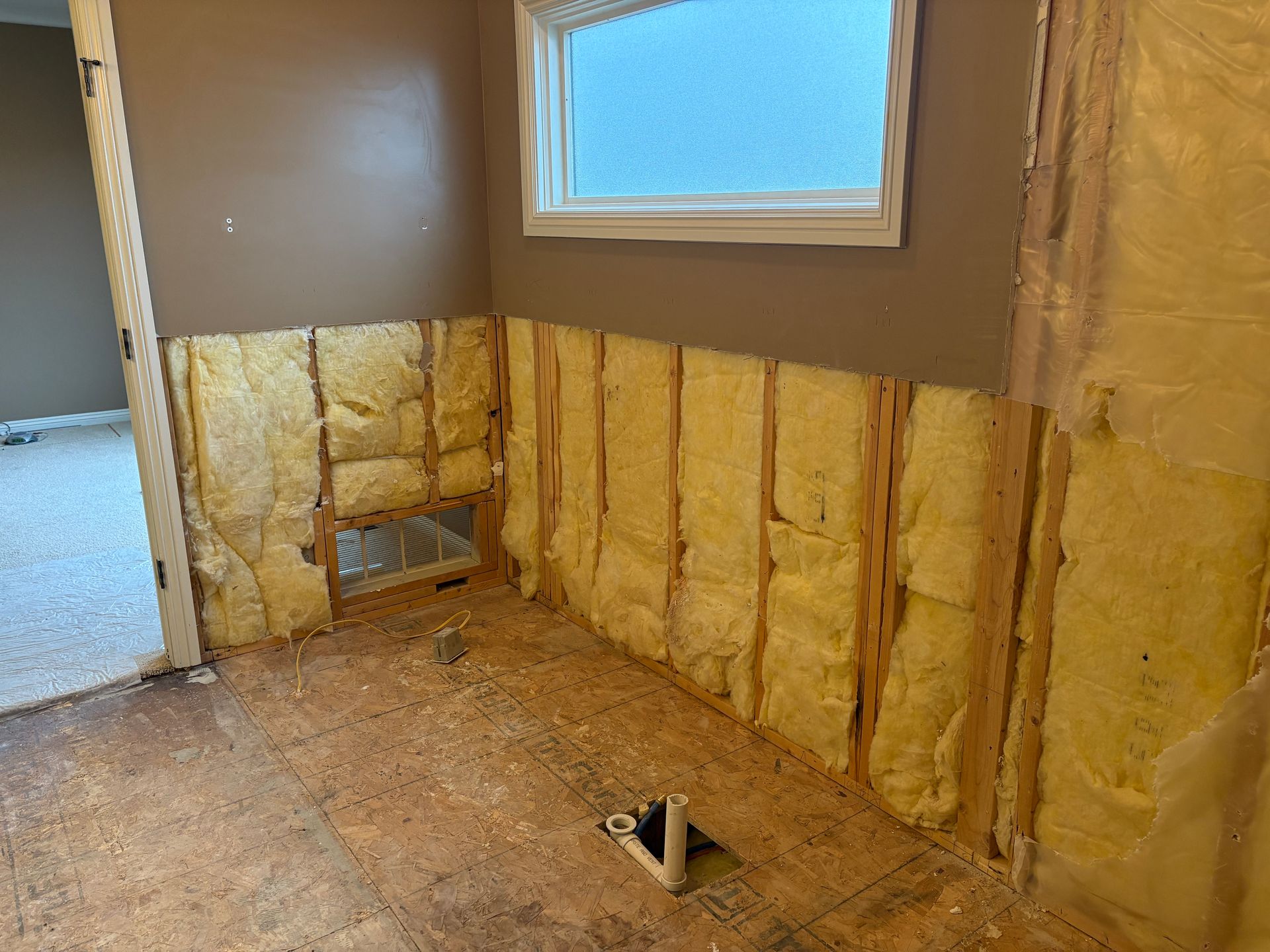 Interior room renovation with exposed insulation and wall studs; near a window.