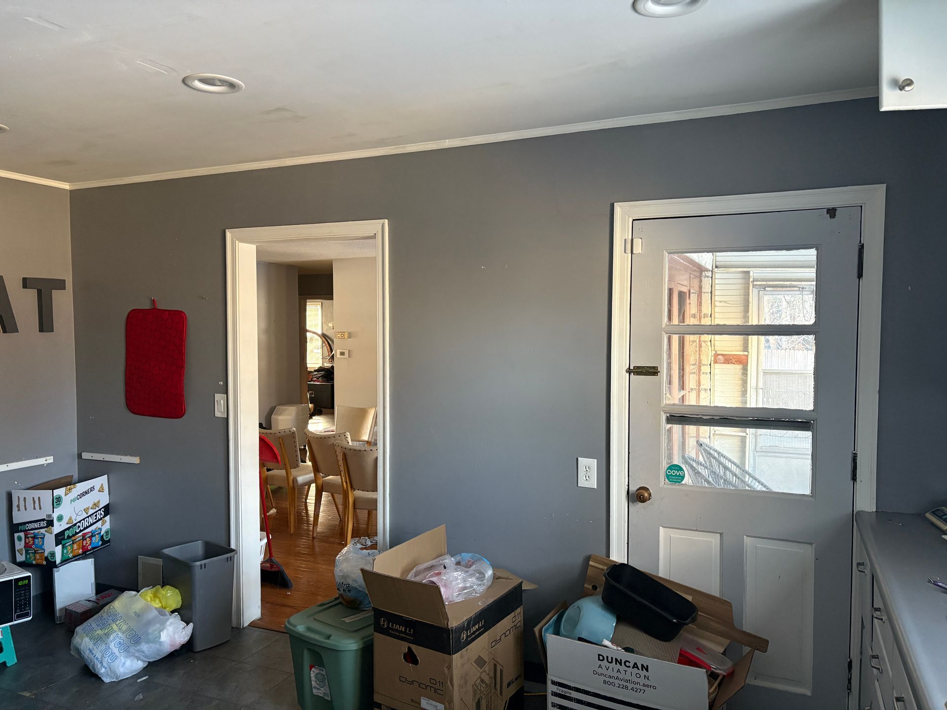 Interior kitchen with gray walls, cluttered with boxes and a door leading outside.