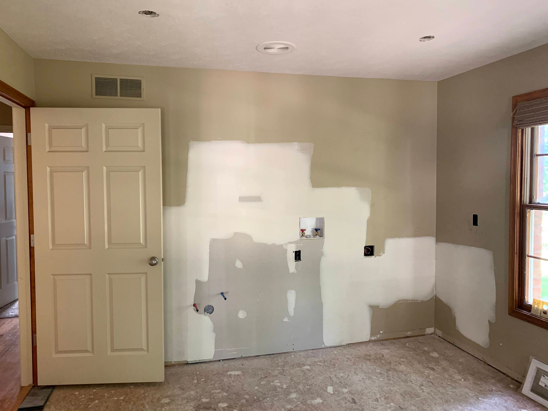 Room with beige walls, unfinished drywall, a white door, and a window.