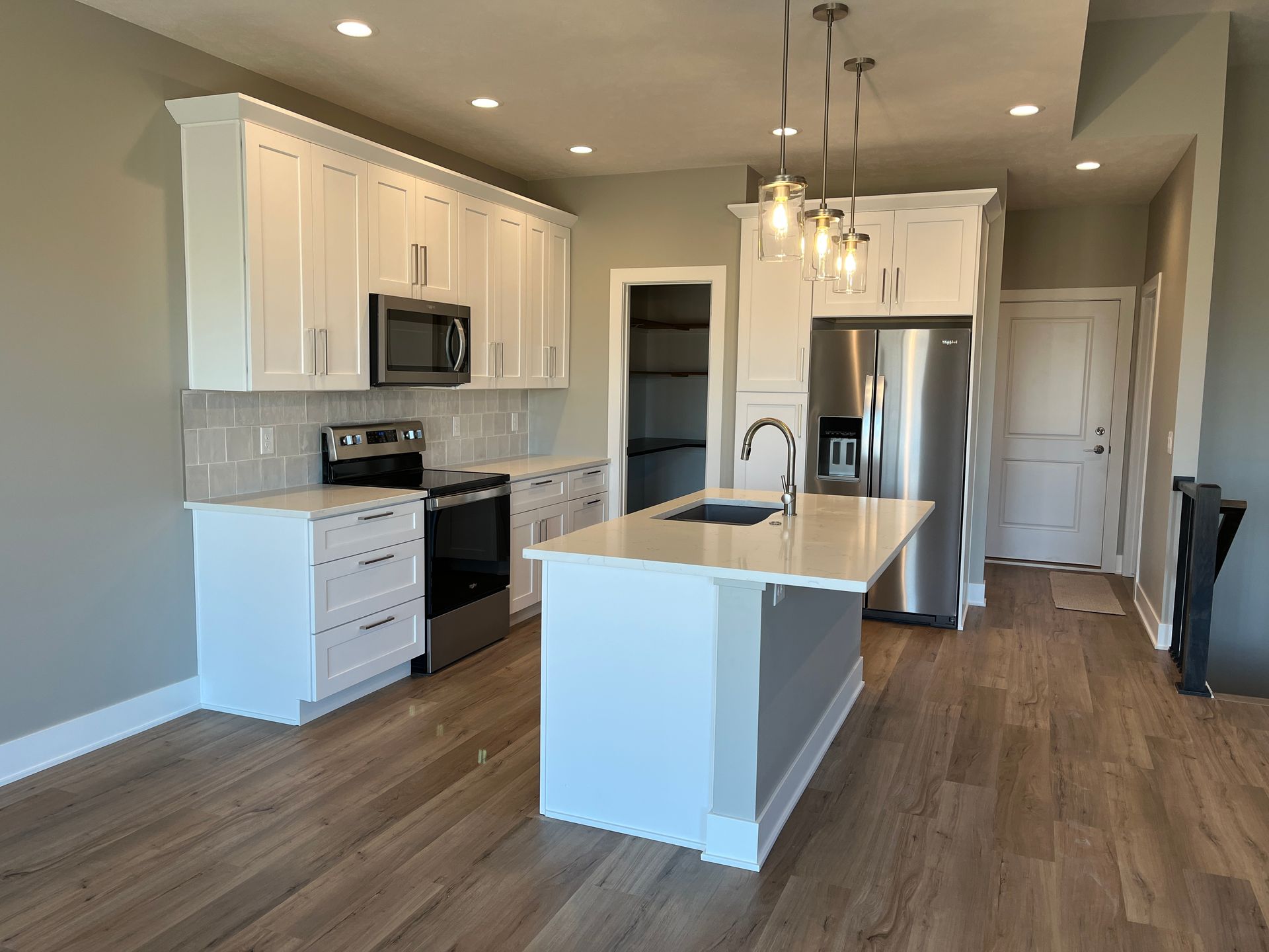 A kitchen with white cabinets , stainless steel appliances , and a large island.