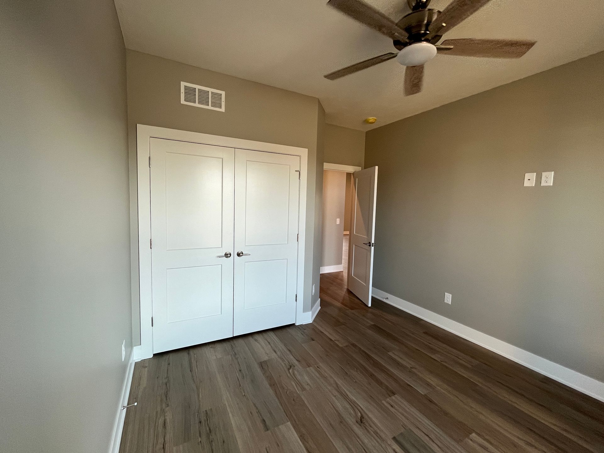 An empty bedroom with hardwood floors and a ceiling fan.
