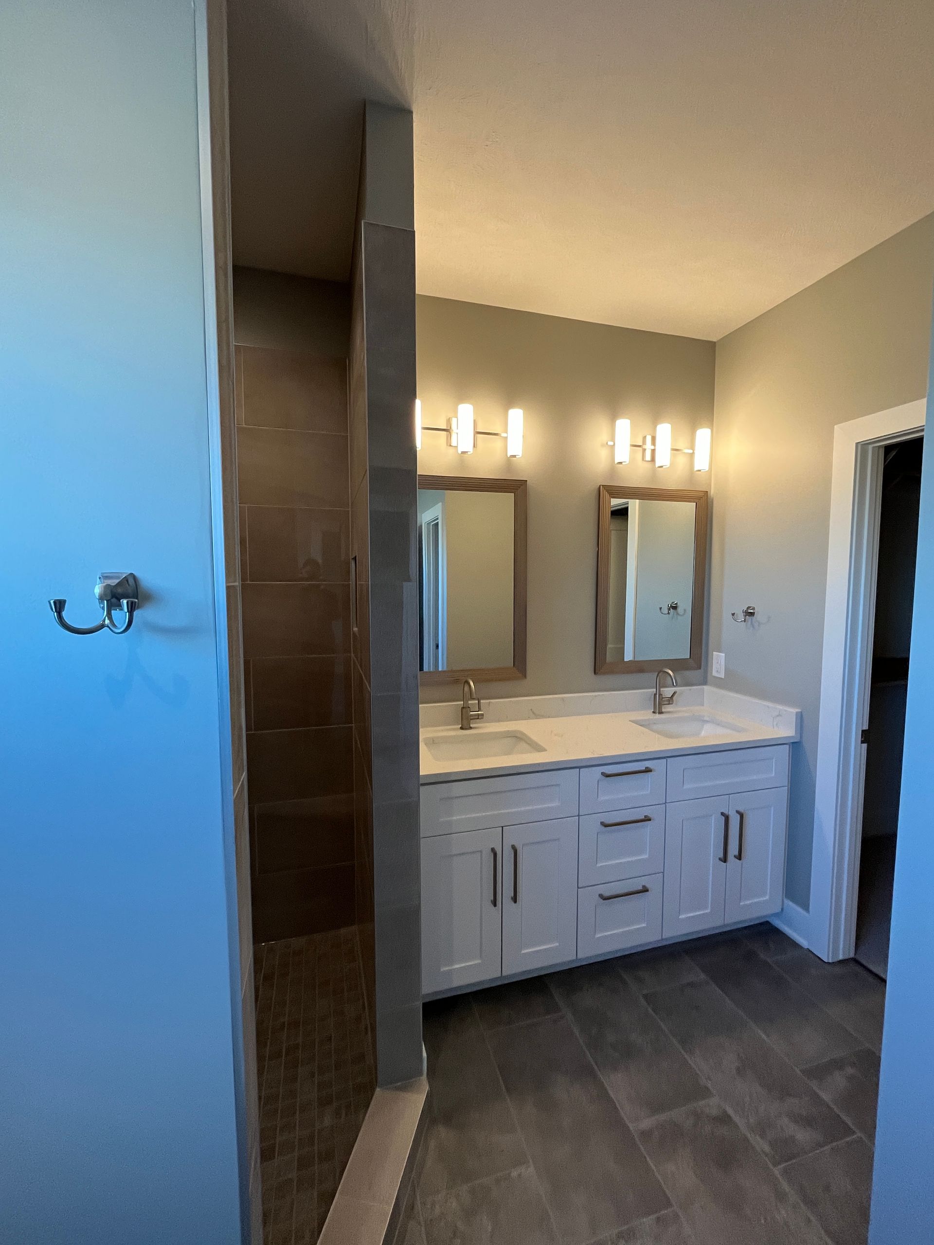 A bathroom with two sinks , two mirrors and a walk in shower.