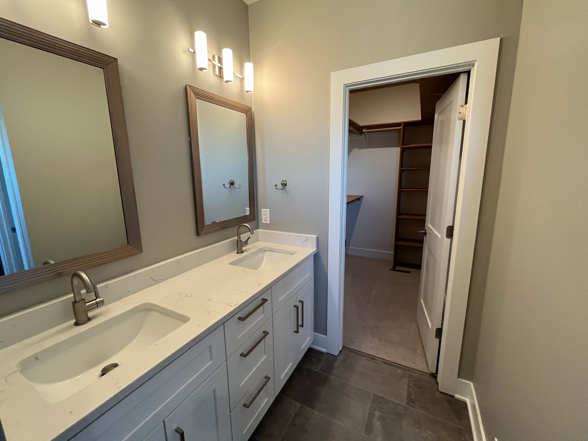 A bathroom with two sinks , two mirrors and a walk in closet.