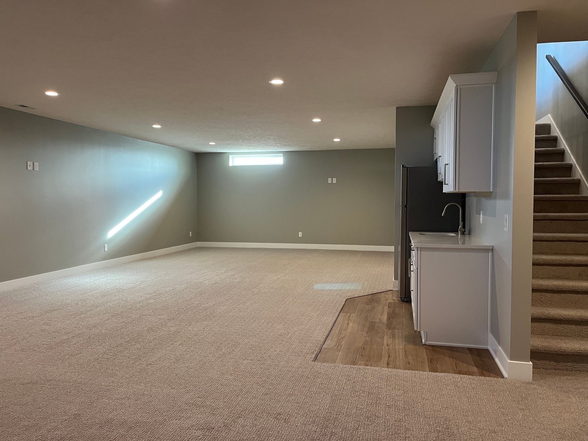 An empty basement with carpeted floors and stairs leading up to the second floor.