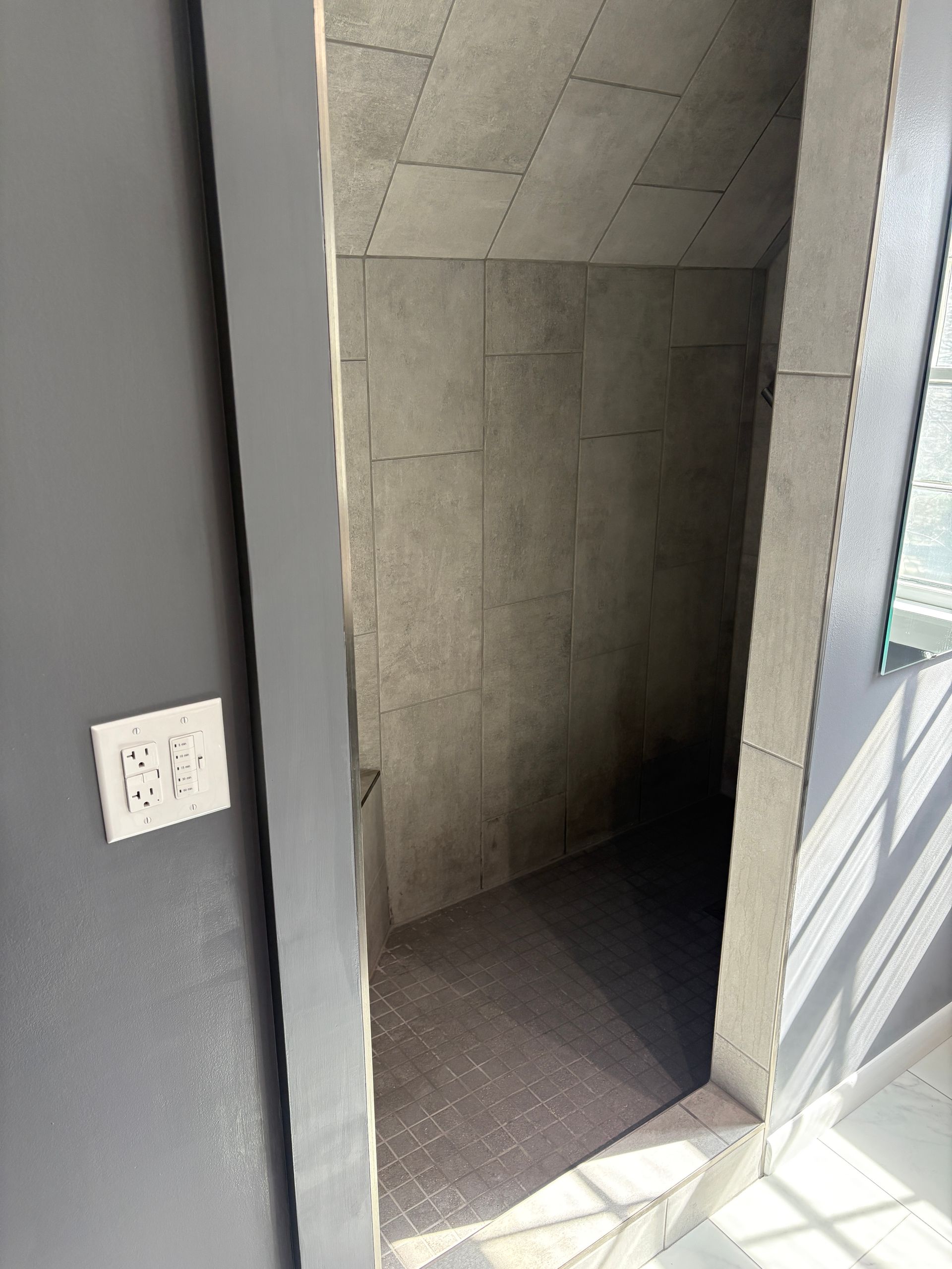 A narrow storage closet with gray walls and dark floor. A light switch is on the gray wall.