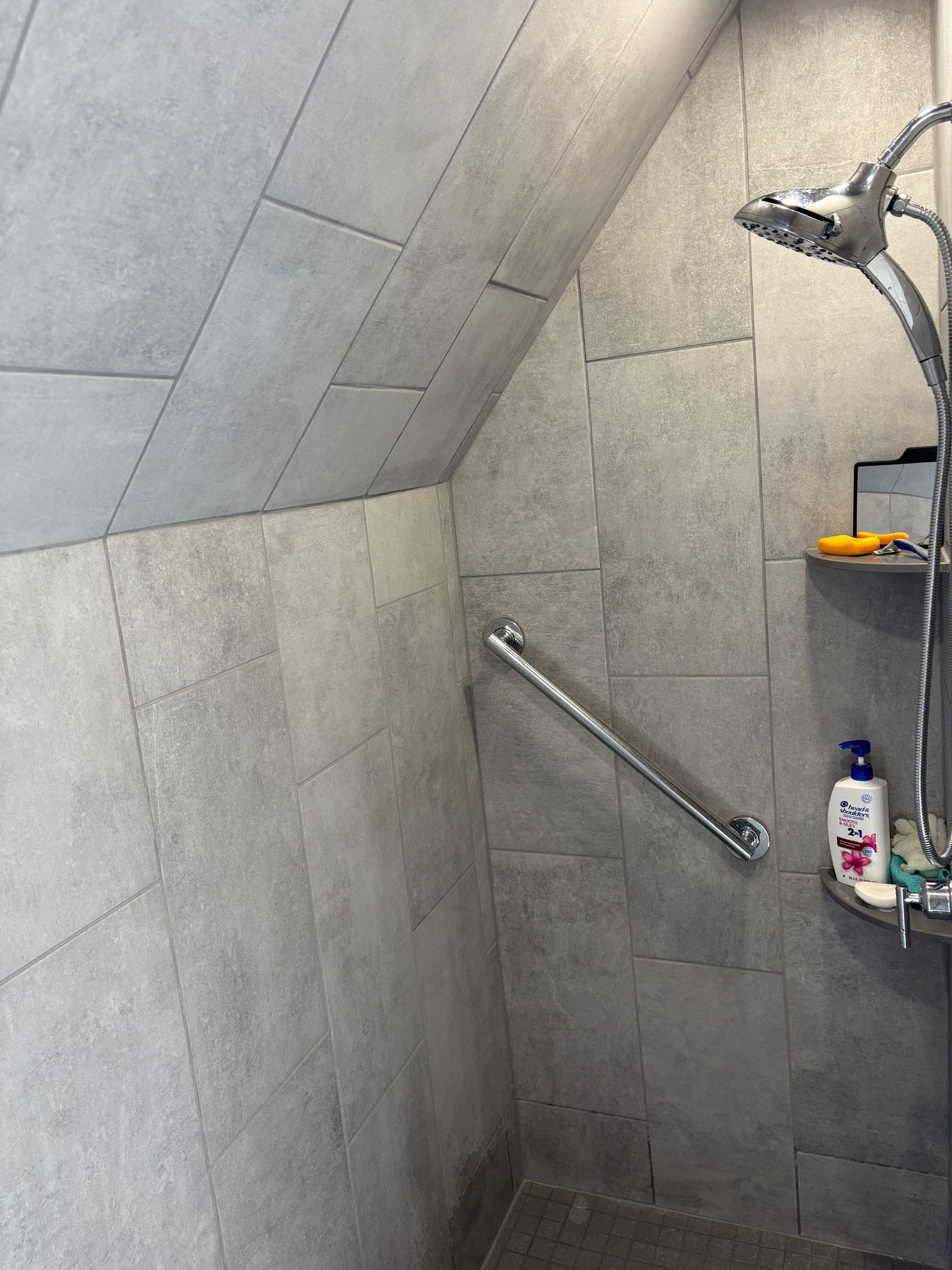 Shower with gray tiled walls, a grab bar, and a showerhead.