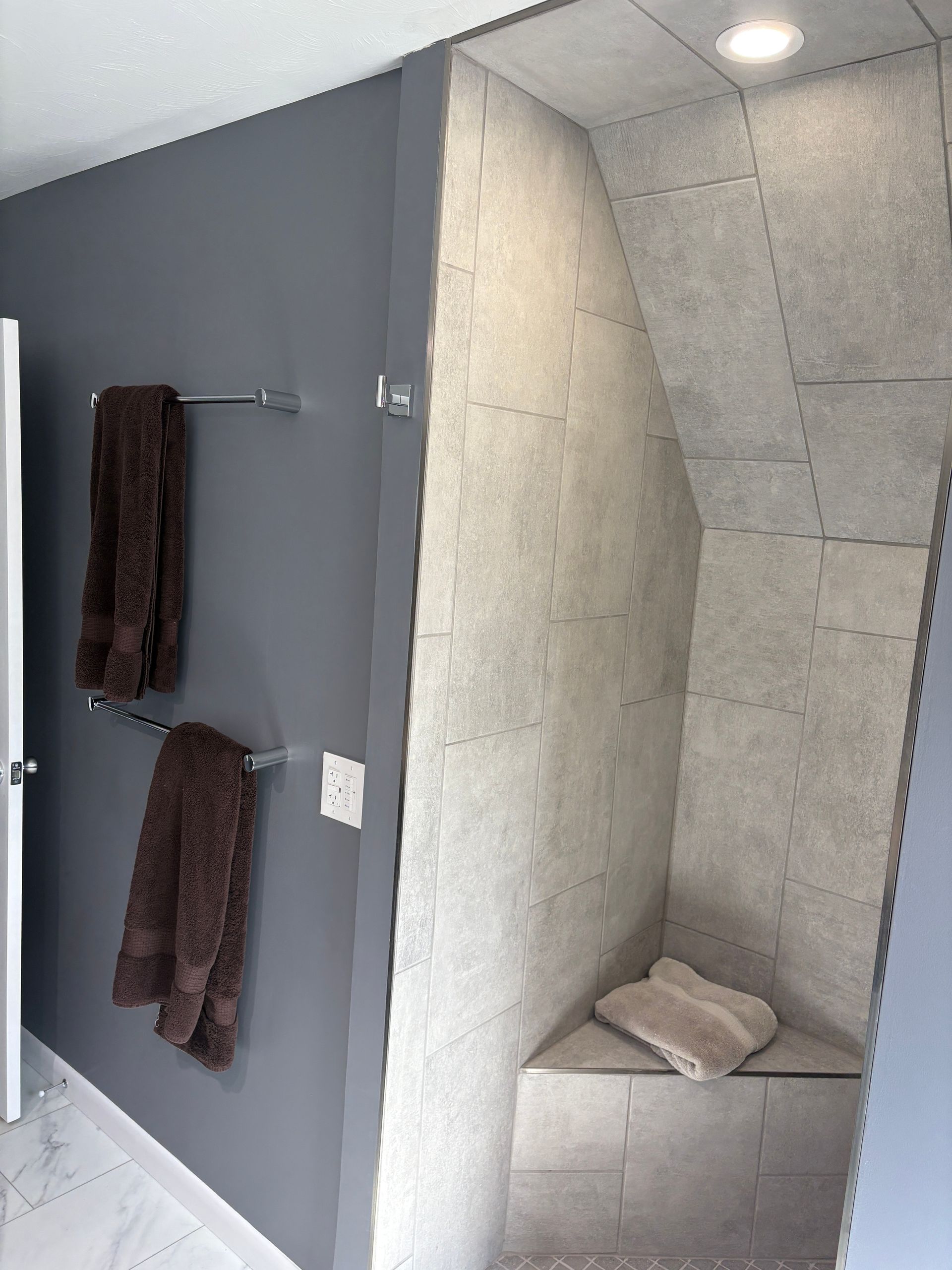 Bathroom with gray walls, towel rack with brown towels, shower with bench.