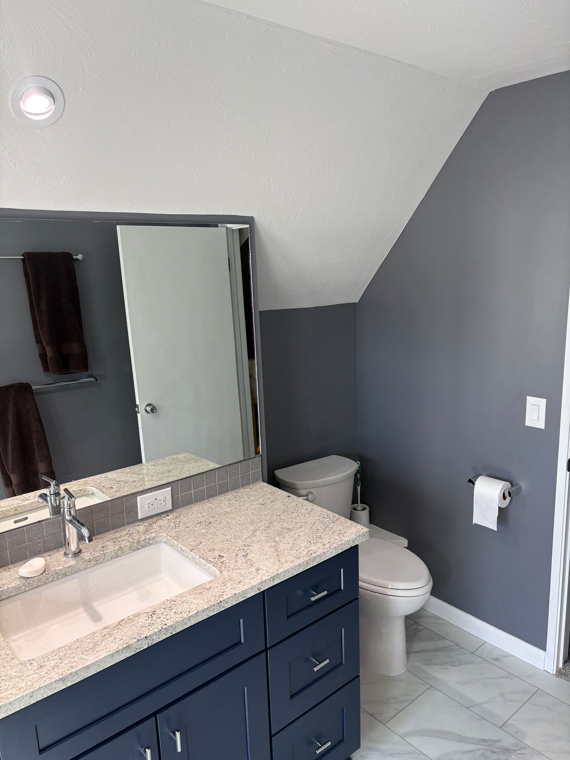 Bathroom with blue vanity, white toilet, gray walls, and marble floor.