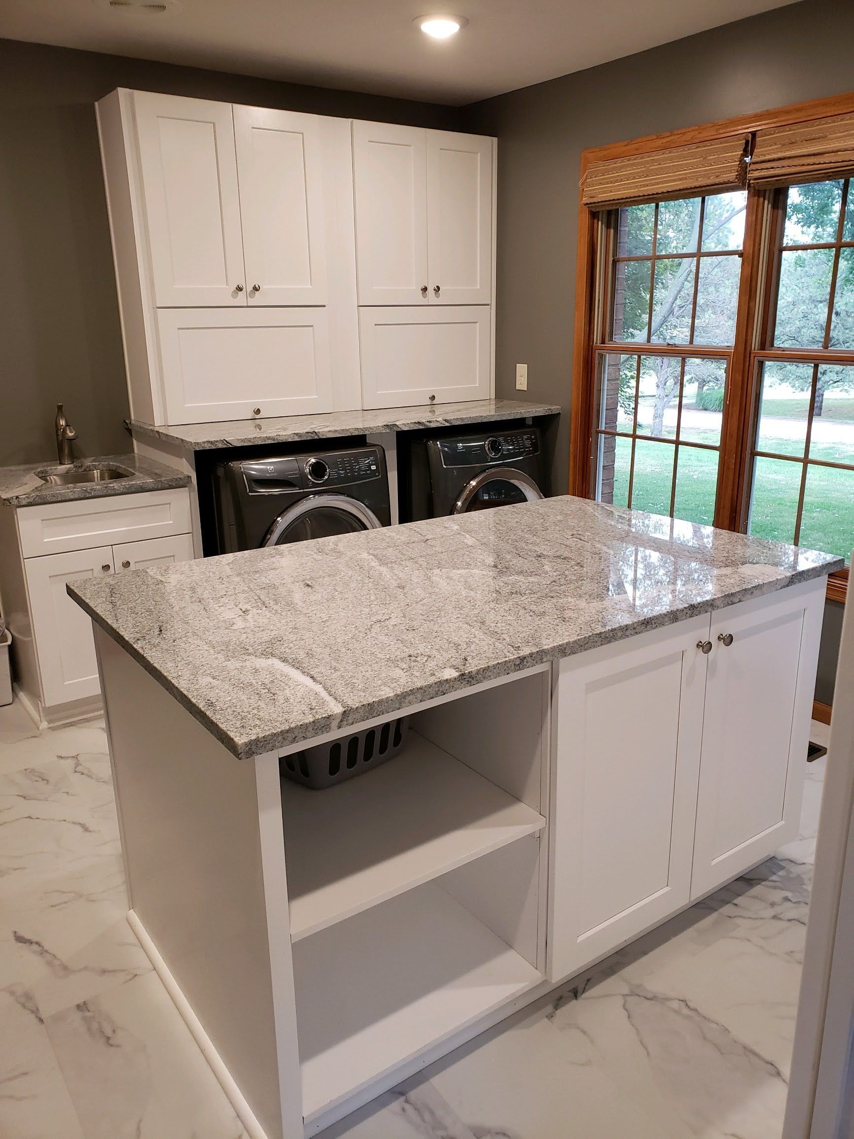 White laundry room with island and granite countertop, washer/dryer, cabinets, and window.