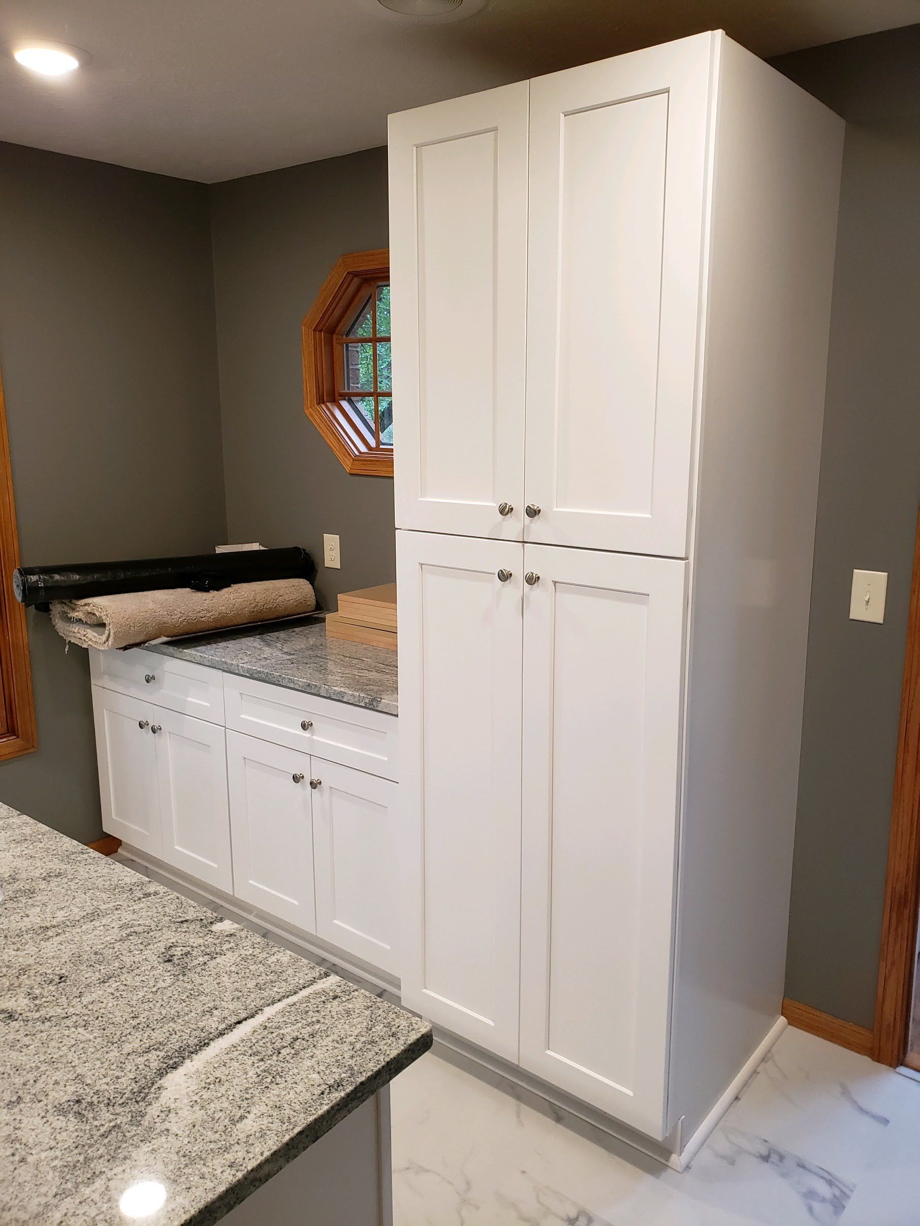 White cabinets, granite countertop, and an oval window in a kitchen.