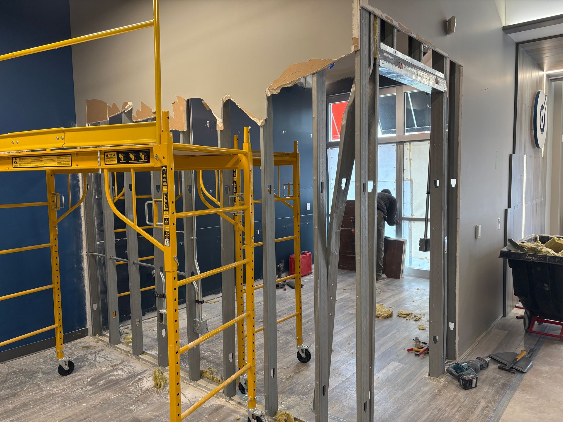 Construction site: doorway demolition with scaffolding, blue wall, debris on the floor.