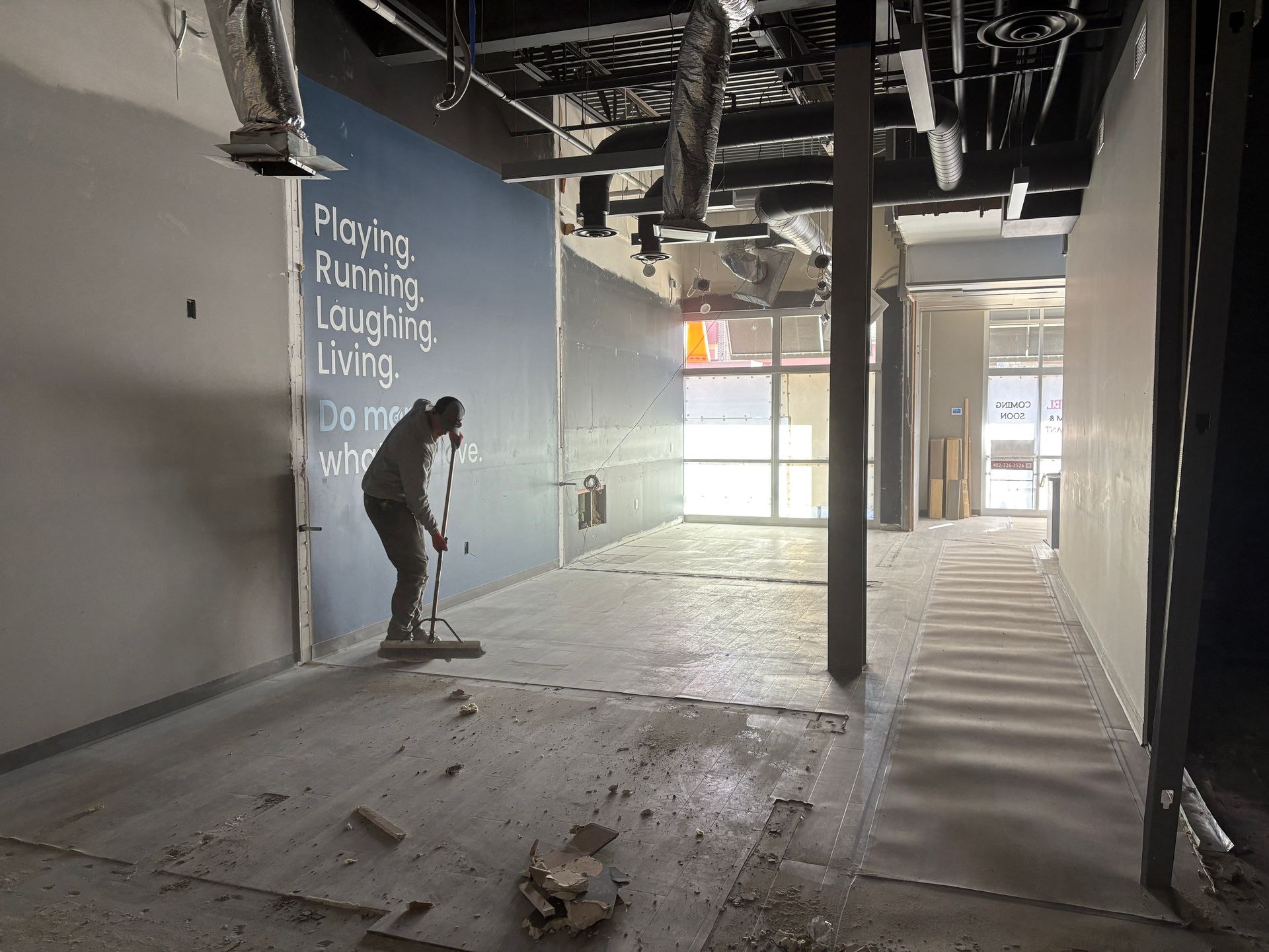 A person sweeping debris in a construction zone with blue and white walls and a window in the distance.
