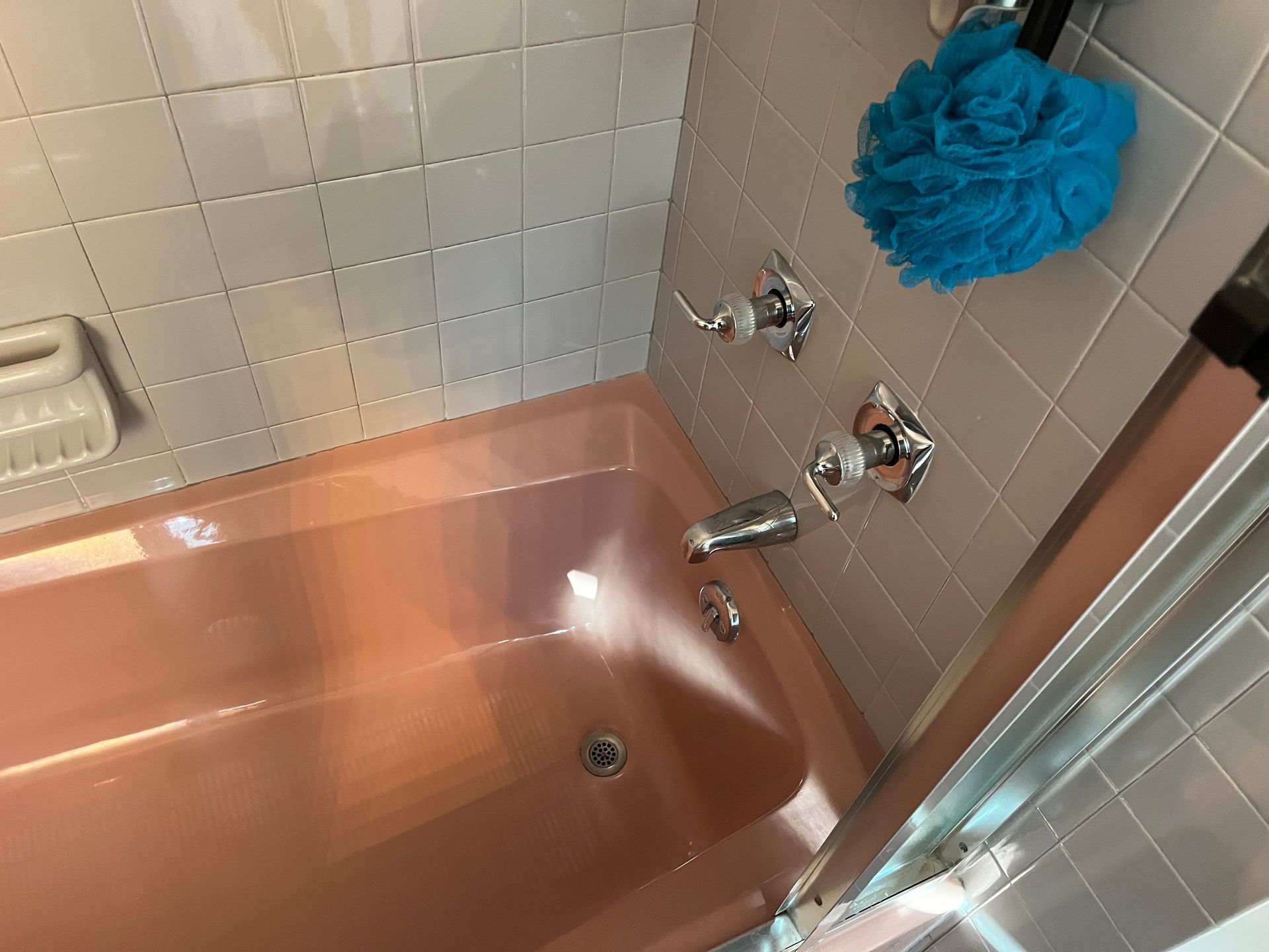 A pink bathtub in a bathroom with a blue sponge hanging on the wall.