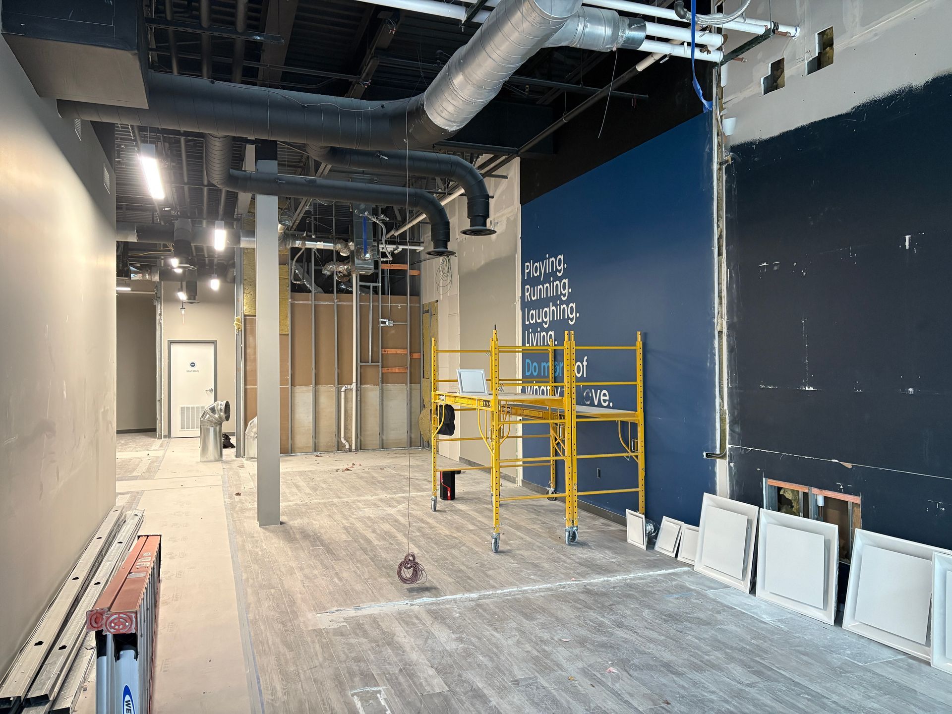 Interior of a building under construction with scaffolding, ductwork, and blue accent wall.