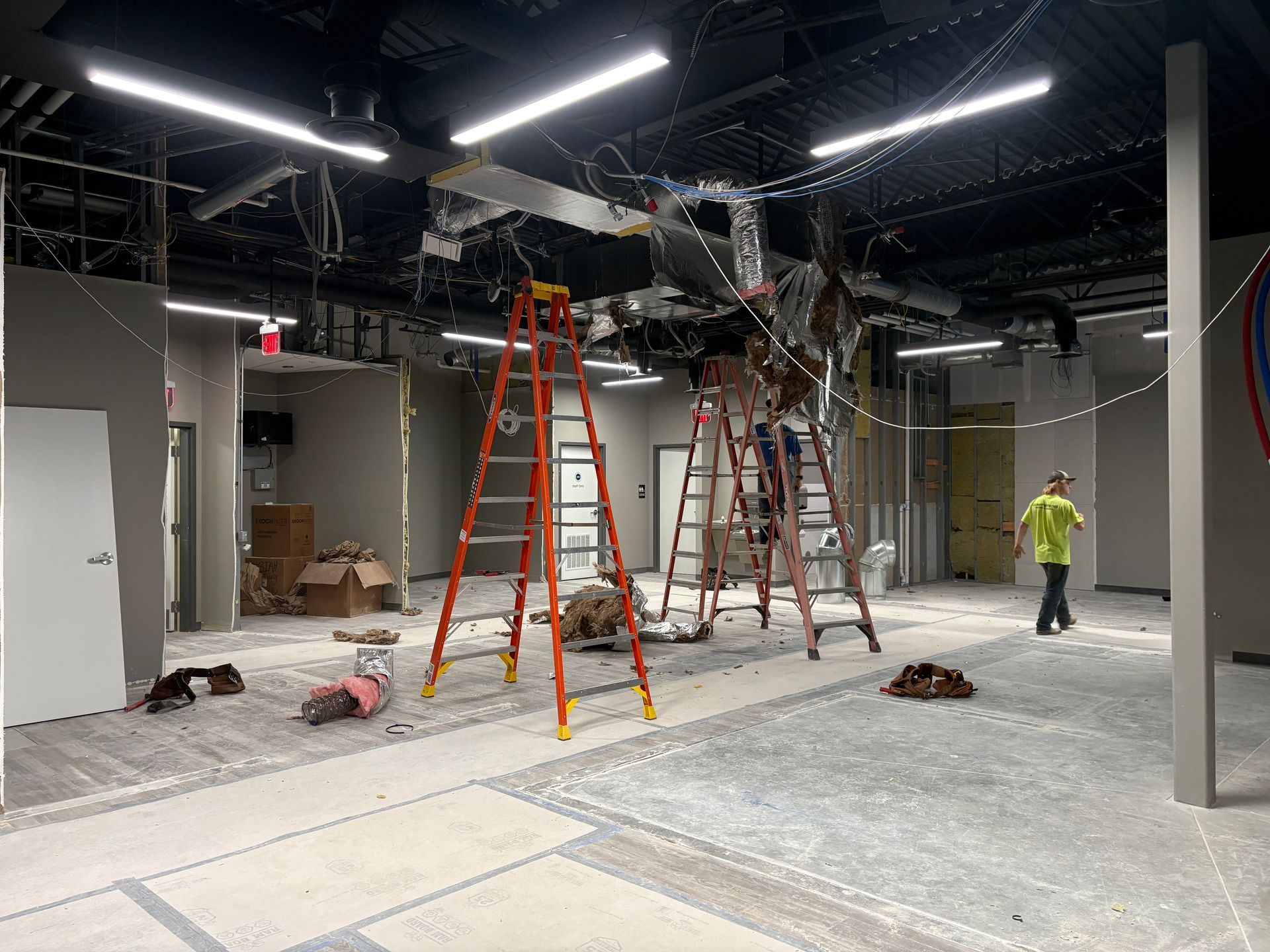Construction site with exposed ceiling, ladders, and workers.