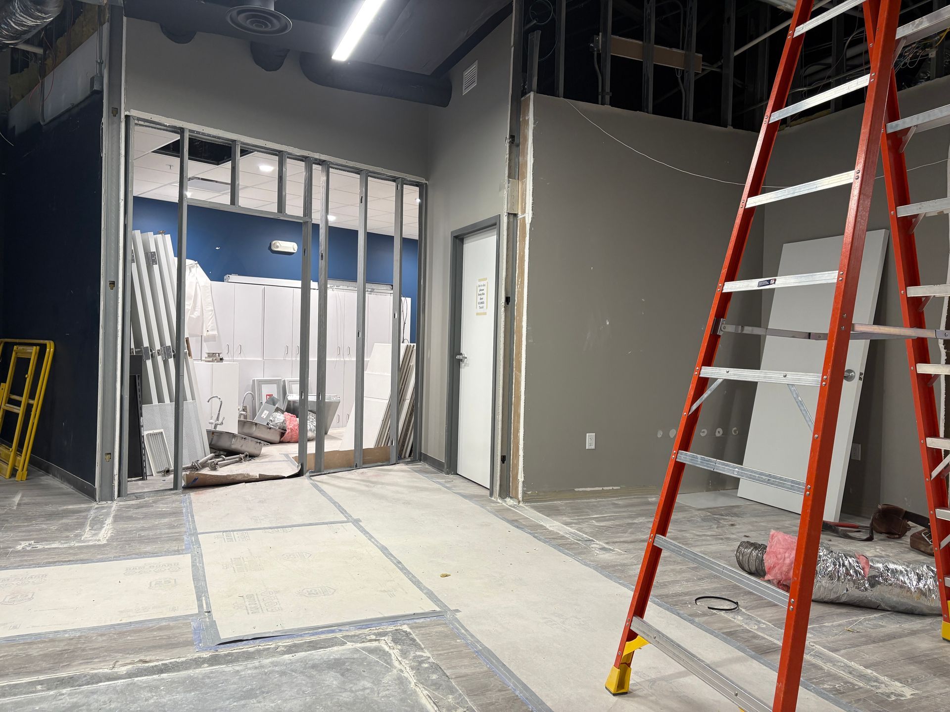 Interior construction site with a ladder, unfinished walls, and a doorway.
