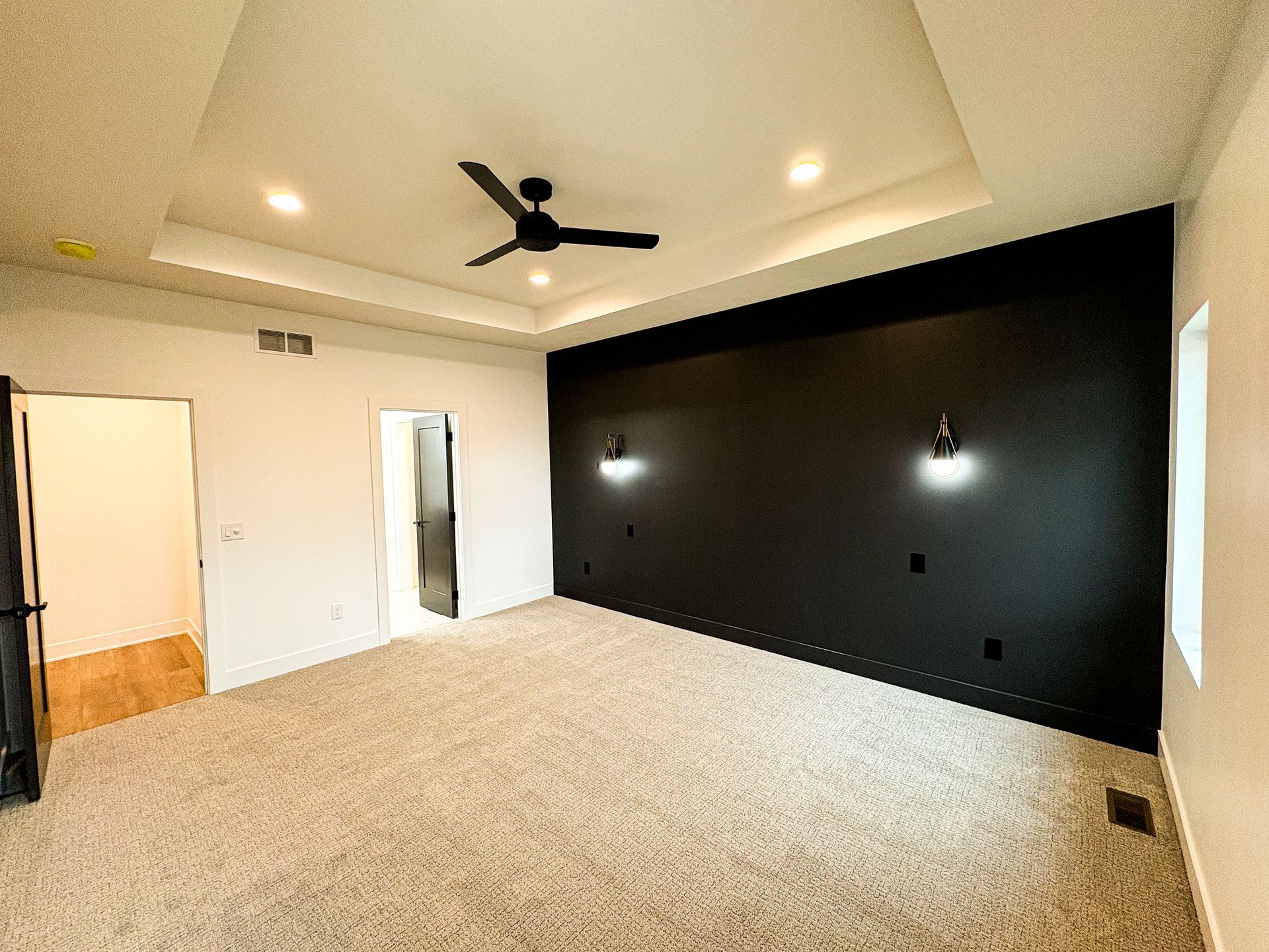Spacious bedroom with carpet, black accent wall, ceiling fan, and recessed lighting. Open doorways.