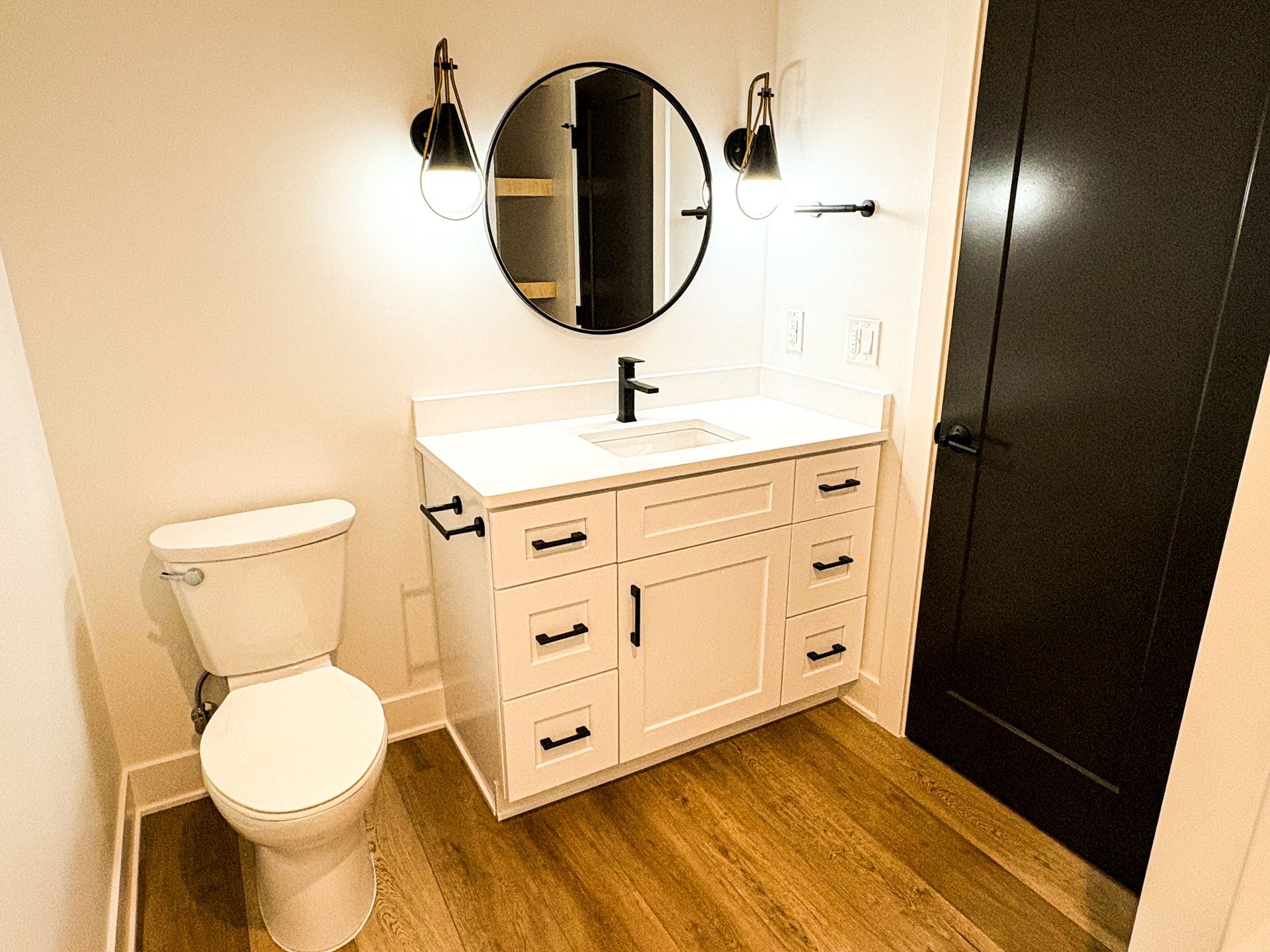 Bathroom with white vanity, black accents, round mirror, and black door.
