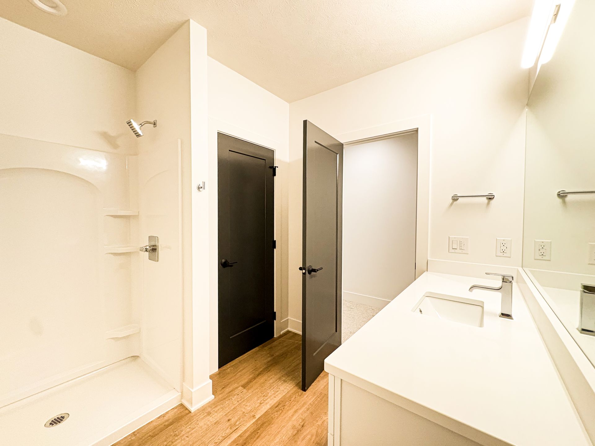 Bathroom with white walls, shower, dark doors, white countertop, and hardwood floors.
