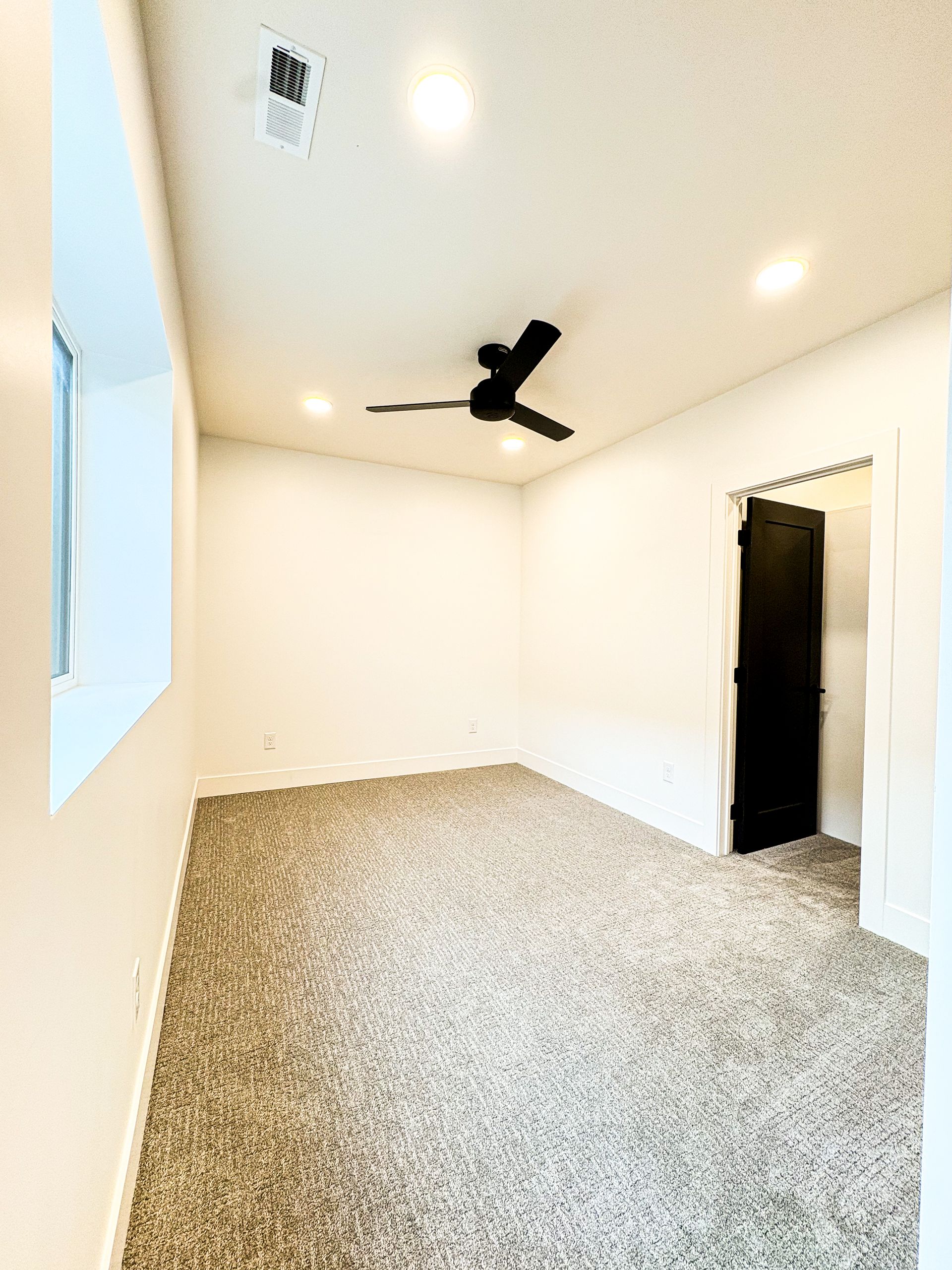 Empty room with neutral carpet, white walls, black ceiling fan, and doorway.