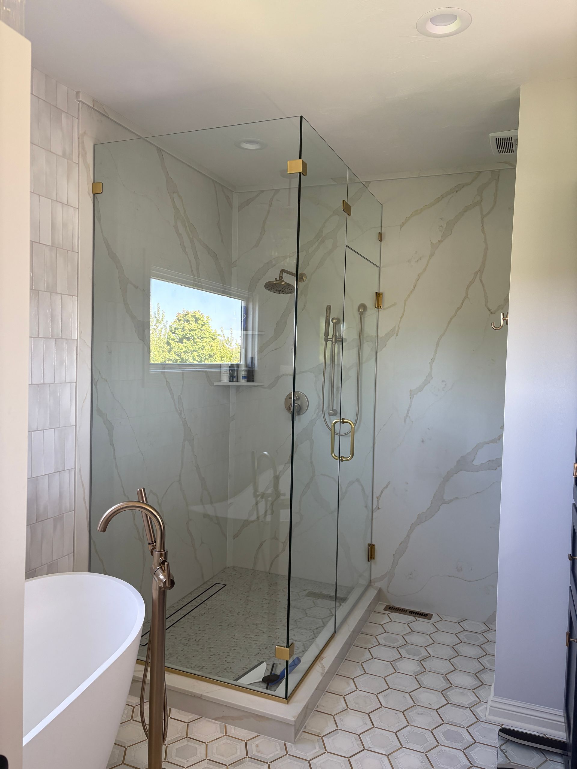 A modern bathroom with a glass shower enclosure, marble tile walls, and hexagon floor tiles.
