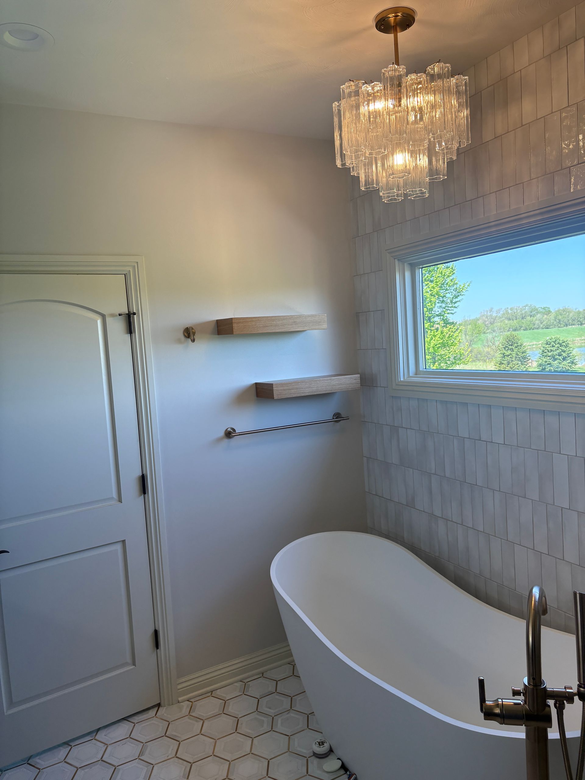 Bright white bathroom with a freestanding tub, chandelier, and window with a view.