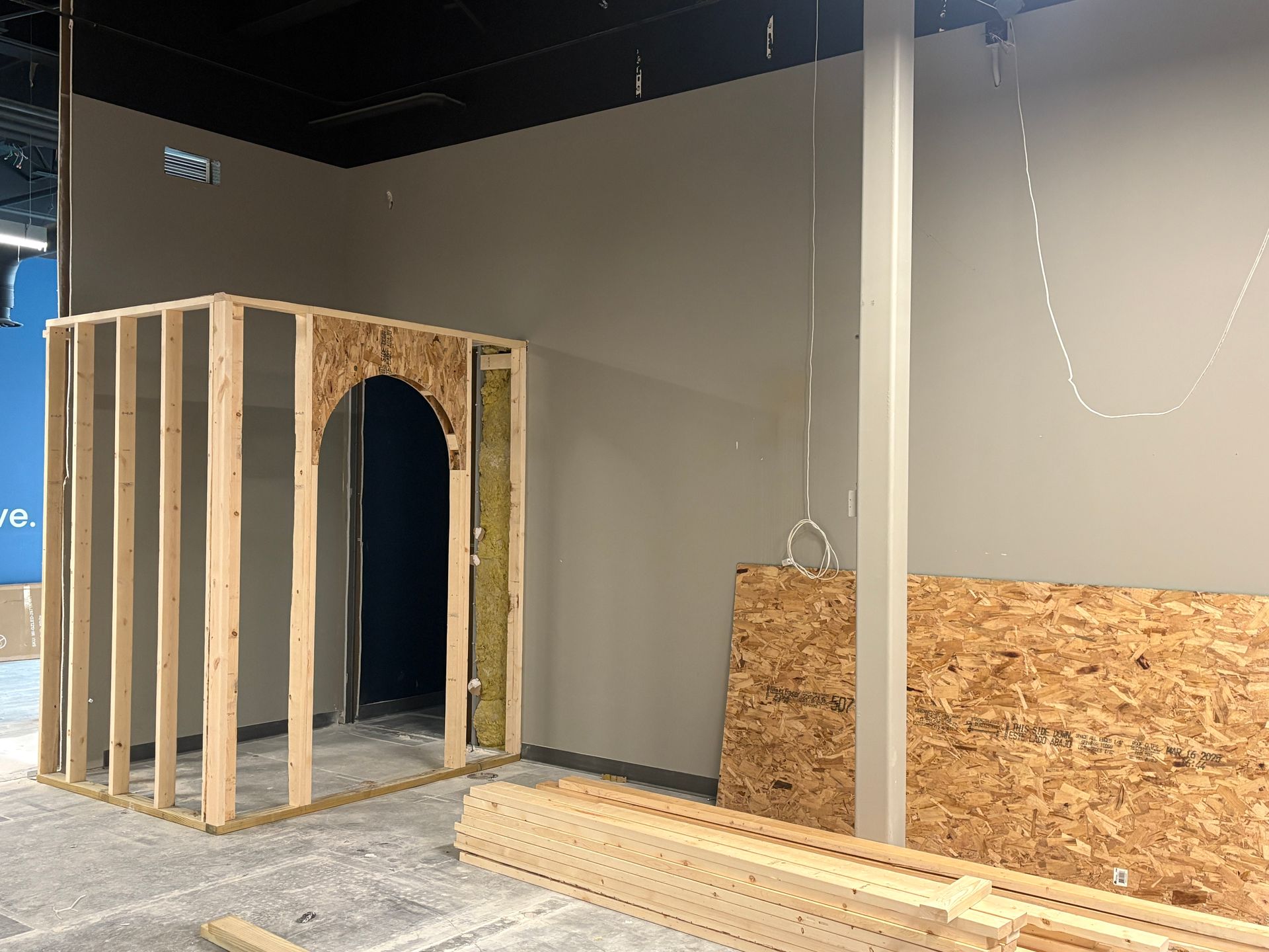 Construction of a room with a wooden frame and arched doorway in a building with gray walls and a black ceiling.
