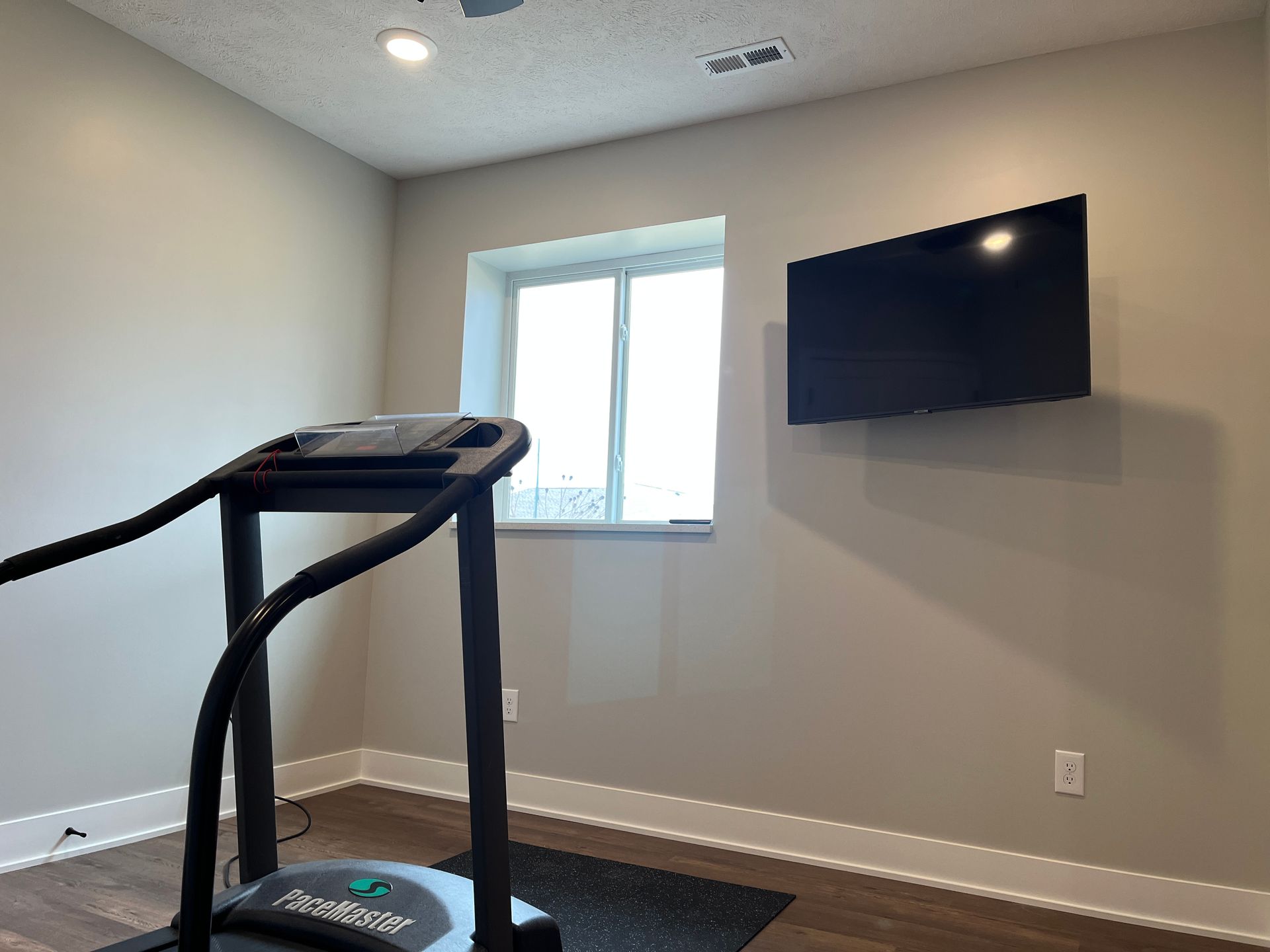 A room with a treadmill and a flat screen tv on the wall.