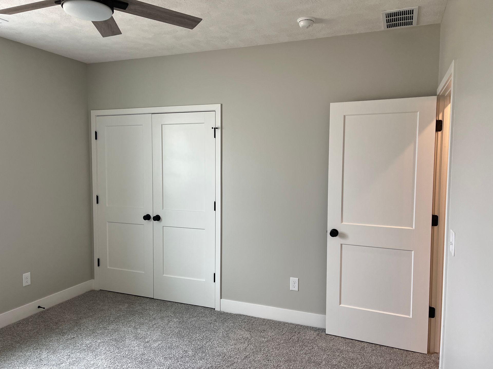 An empty bedroom with two white doors and a ceiling fan.