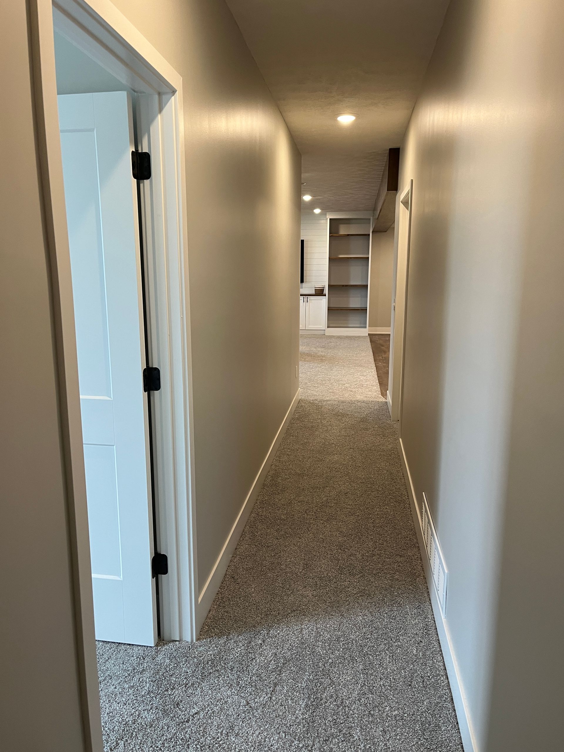 A long hallway with carpeted floors and white walls in a house.