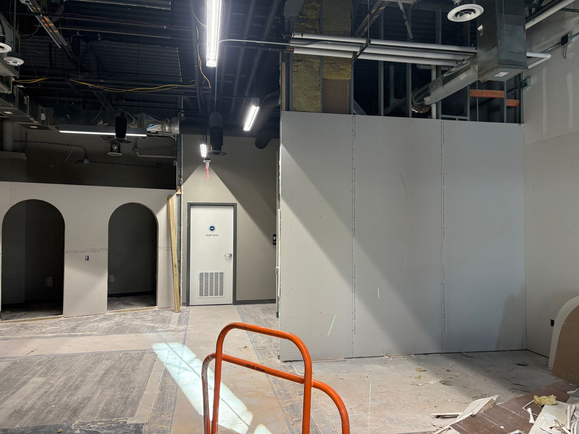 Interior under construction with exposed walls, concrete floor, and an orange hand truck.