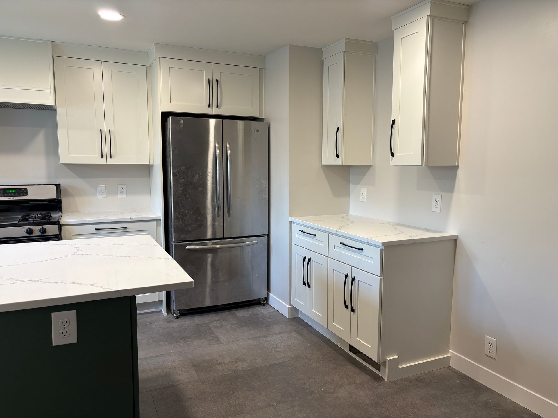 White kitchen with stainless steel fridge, cabinets, and a green island with a white countertop.