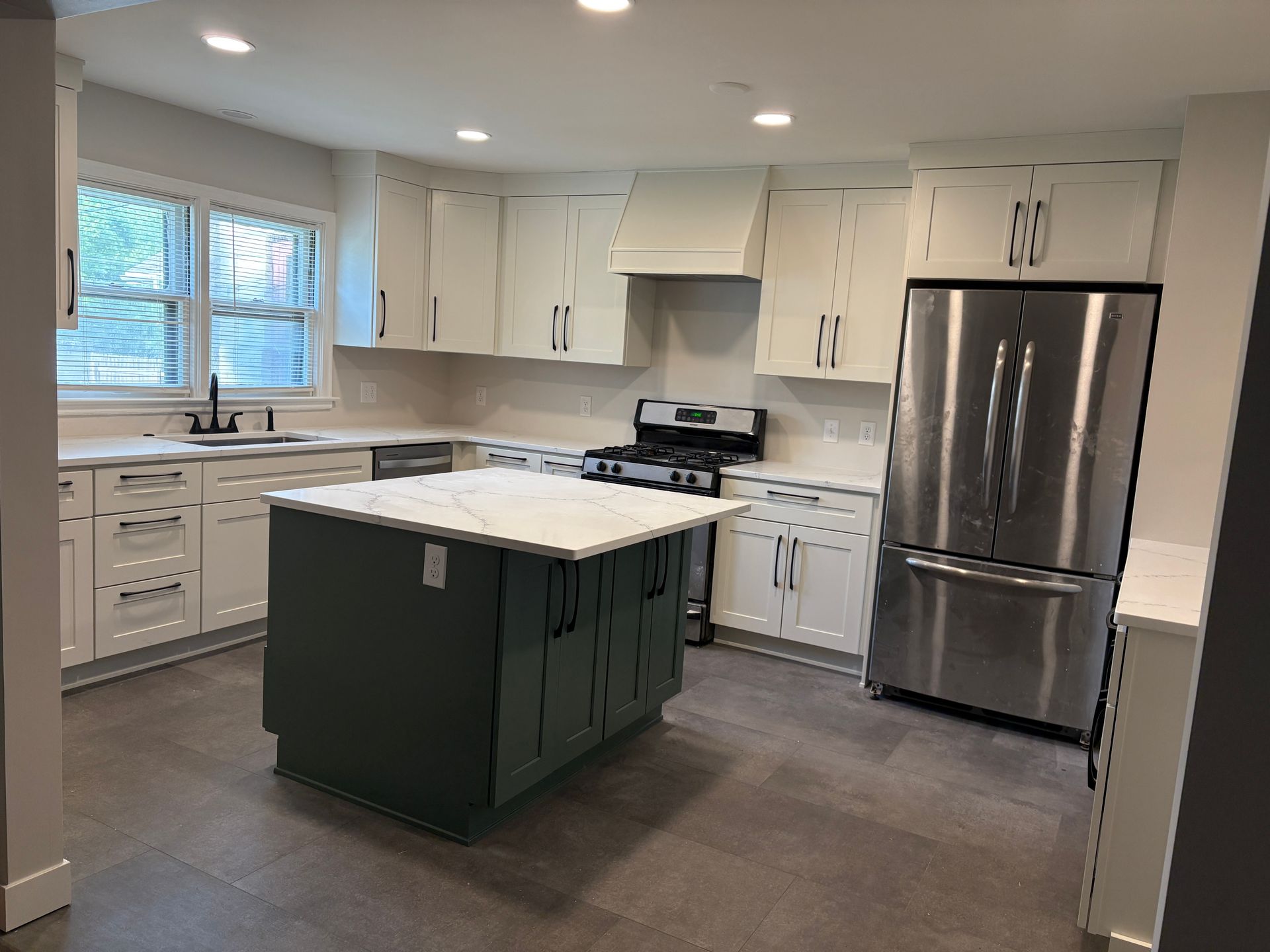 Modern kitchen with white cabinets, green island, stainless steel appliances, and gray tile floor.