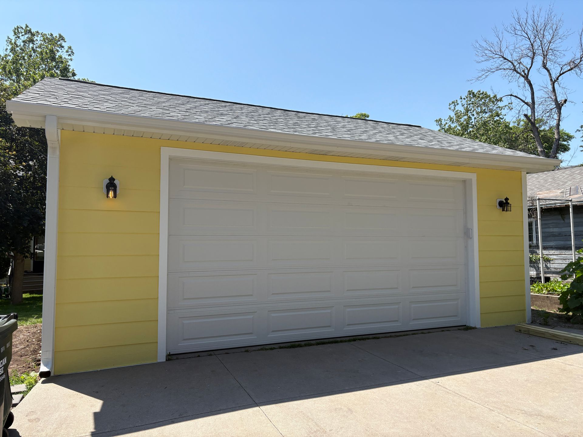 Yellow garage with white door, gray roof, and two black lights, on a concrete pad.