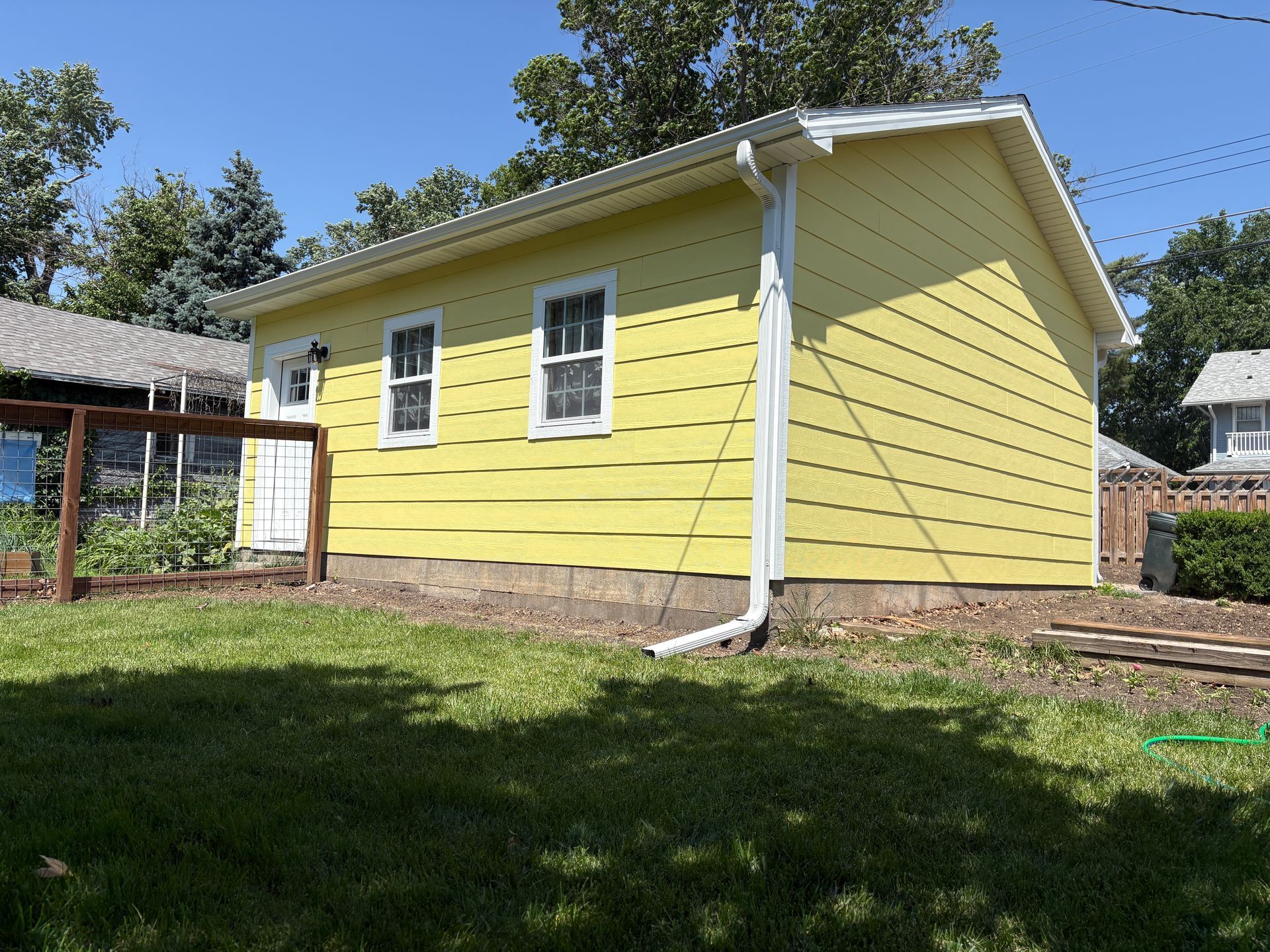 Yellow shed with white trim and windows, on a grassy lot.
