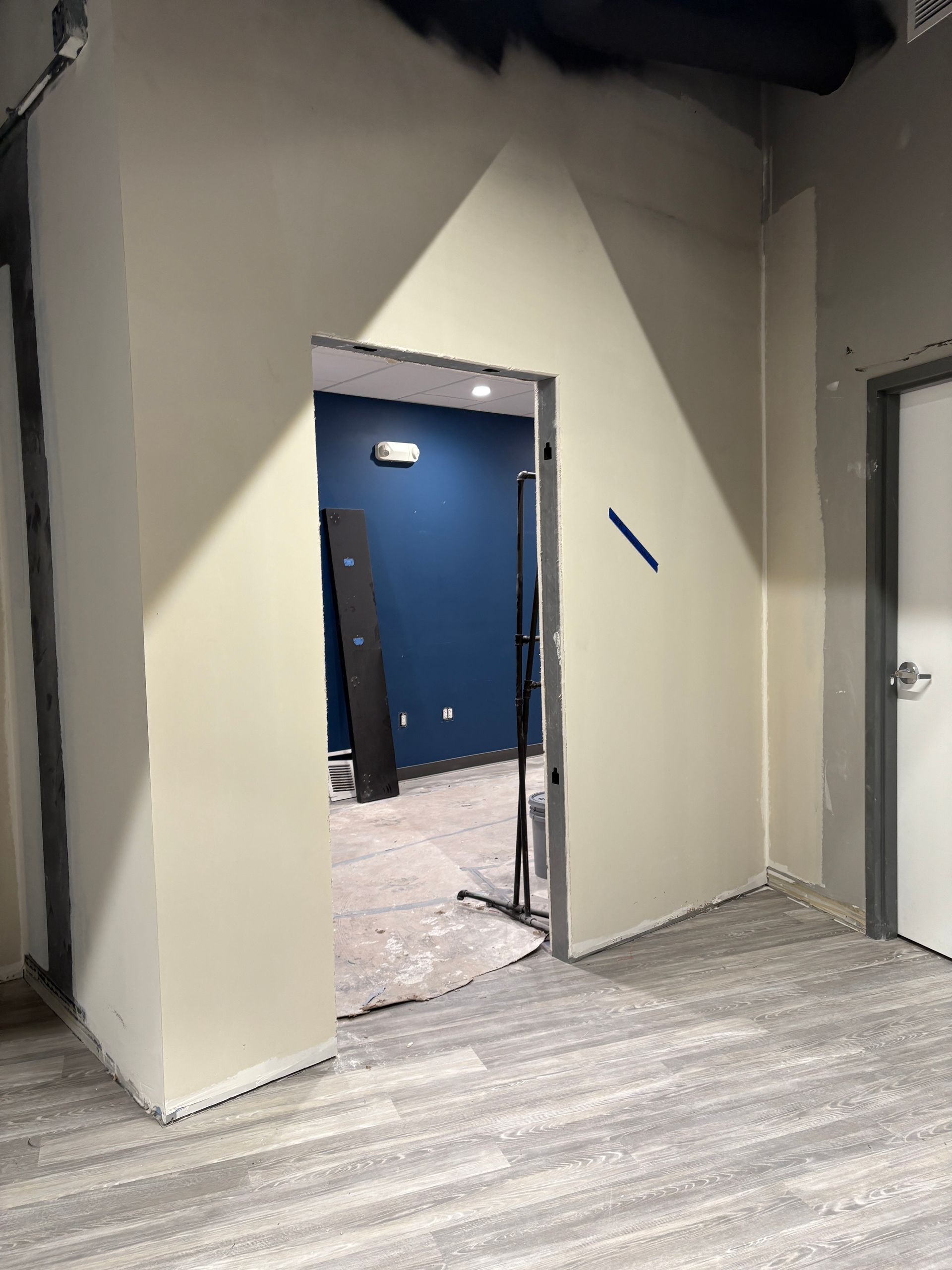 Interior view of a room with an open doorway, beige walls, and a dark blue room visible beyond.