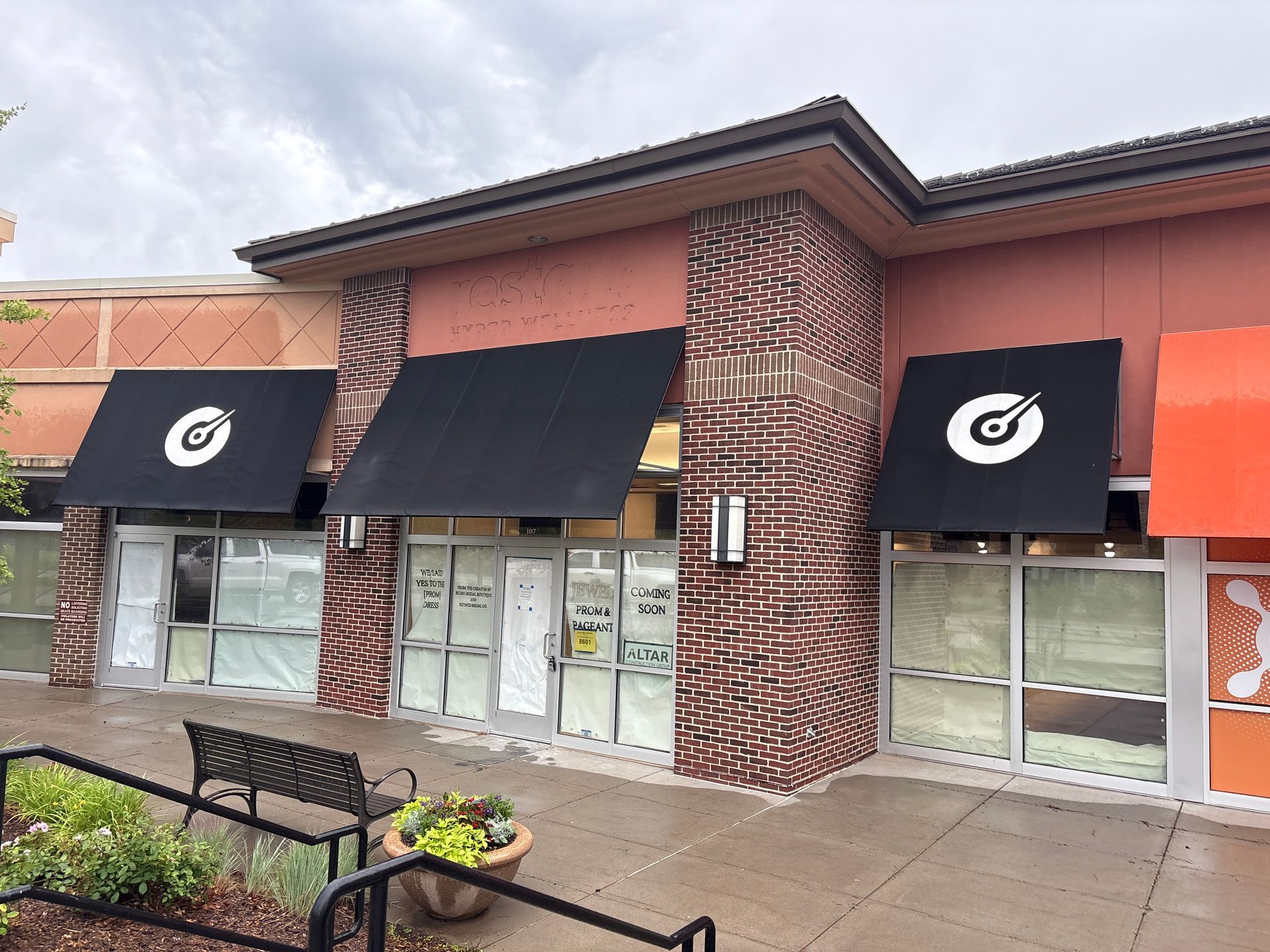 Exterior of a building with closed windows, black awnings, and a logo.