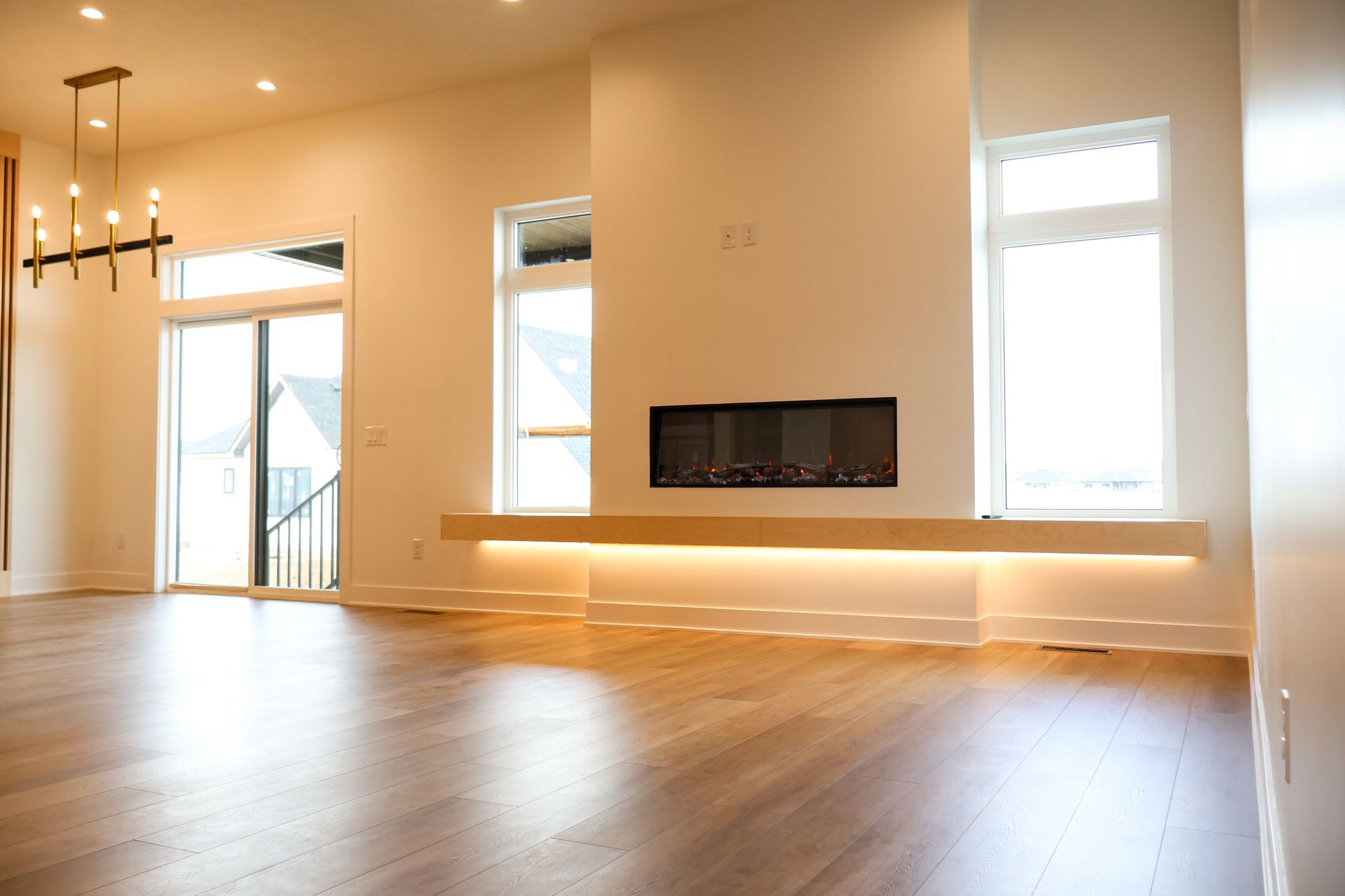 Spacious living room with hardwood floors, a fireplace, and large windows. Warm lighting and a modern chandelier.