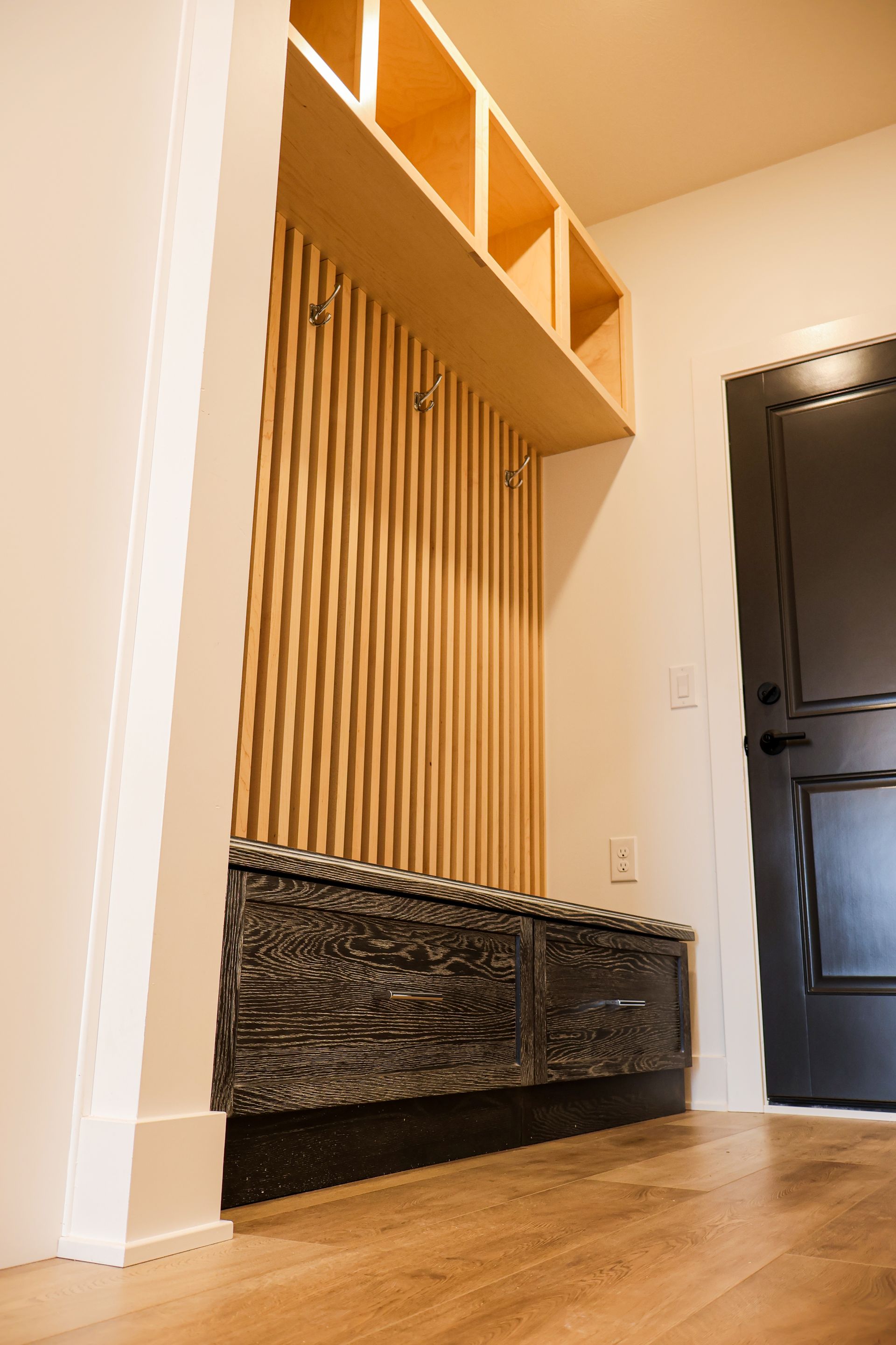 Built-in entryway storage unit with vertical wood paneling, black bench, and open shelves.
