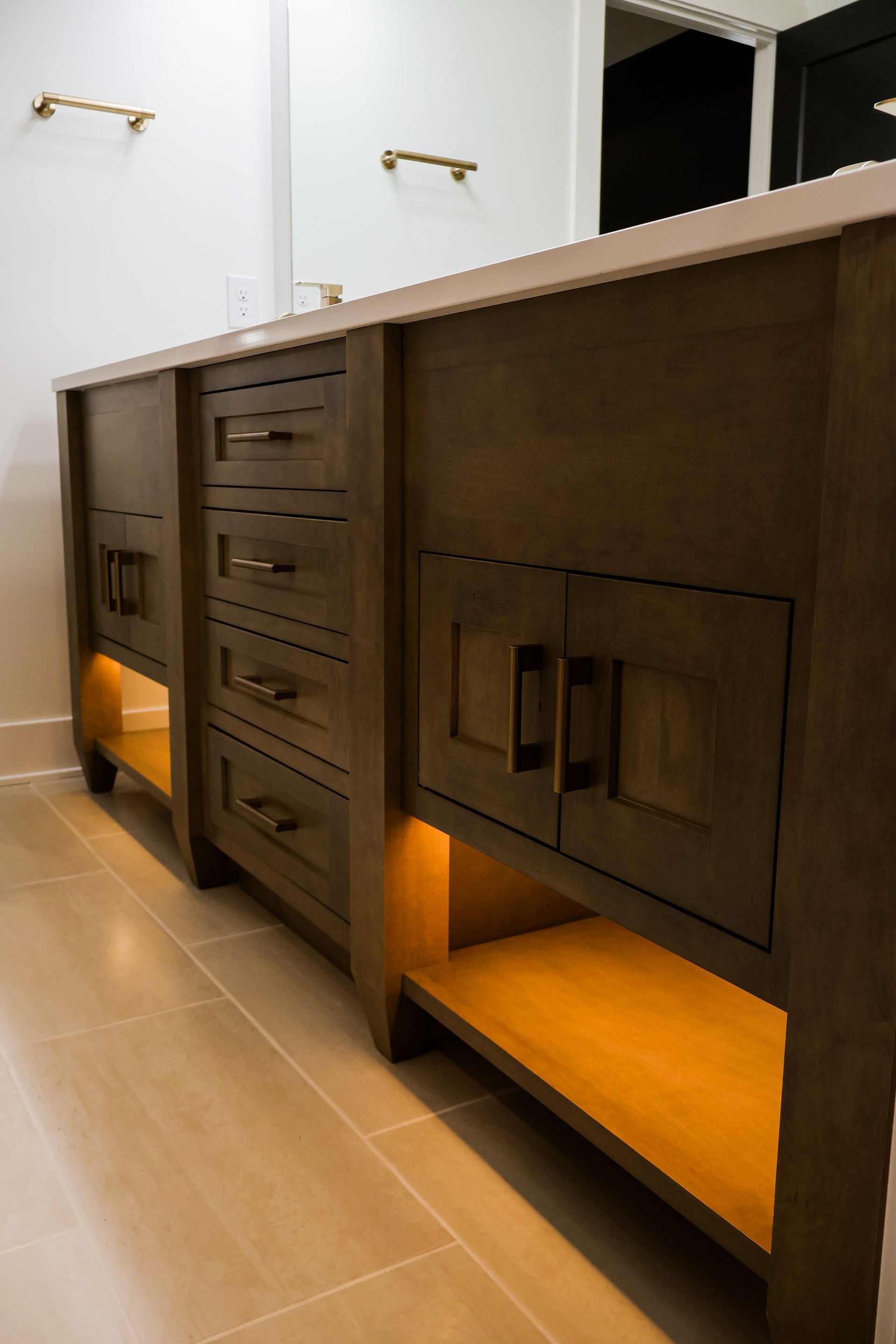 Wooden bathroom vanity with drawers and cabinets, lit from underneath.