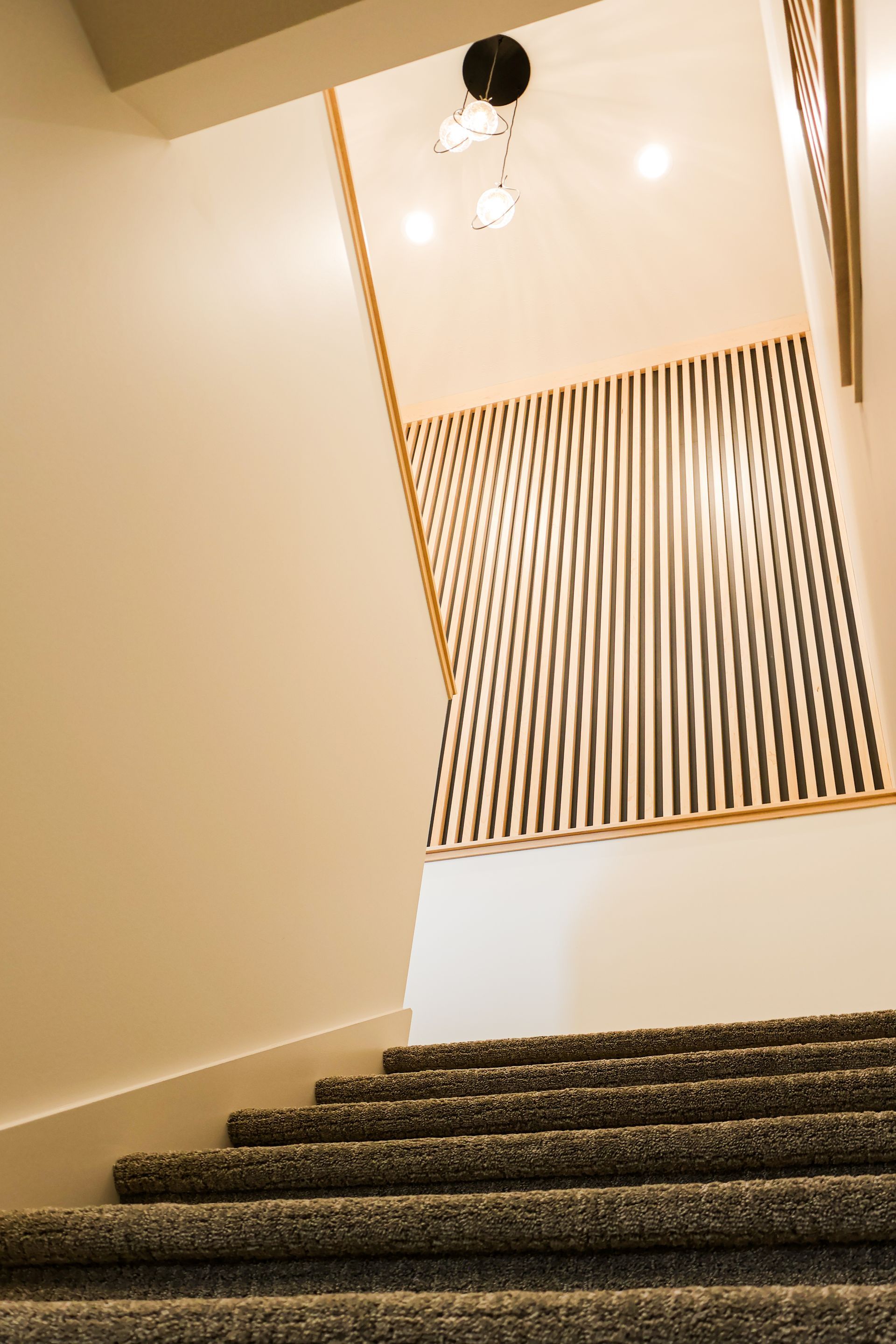 Staircase with textured carpet and wood railing, lit by a modern ceiling fixture.