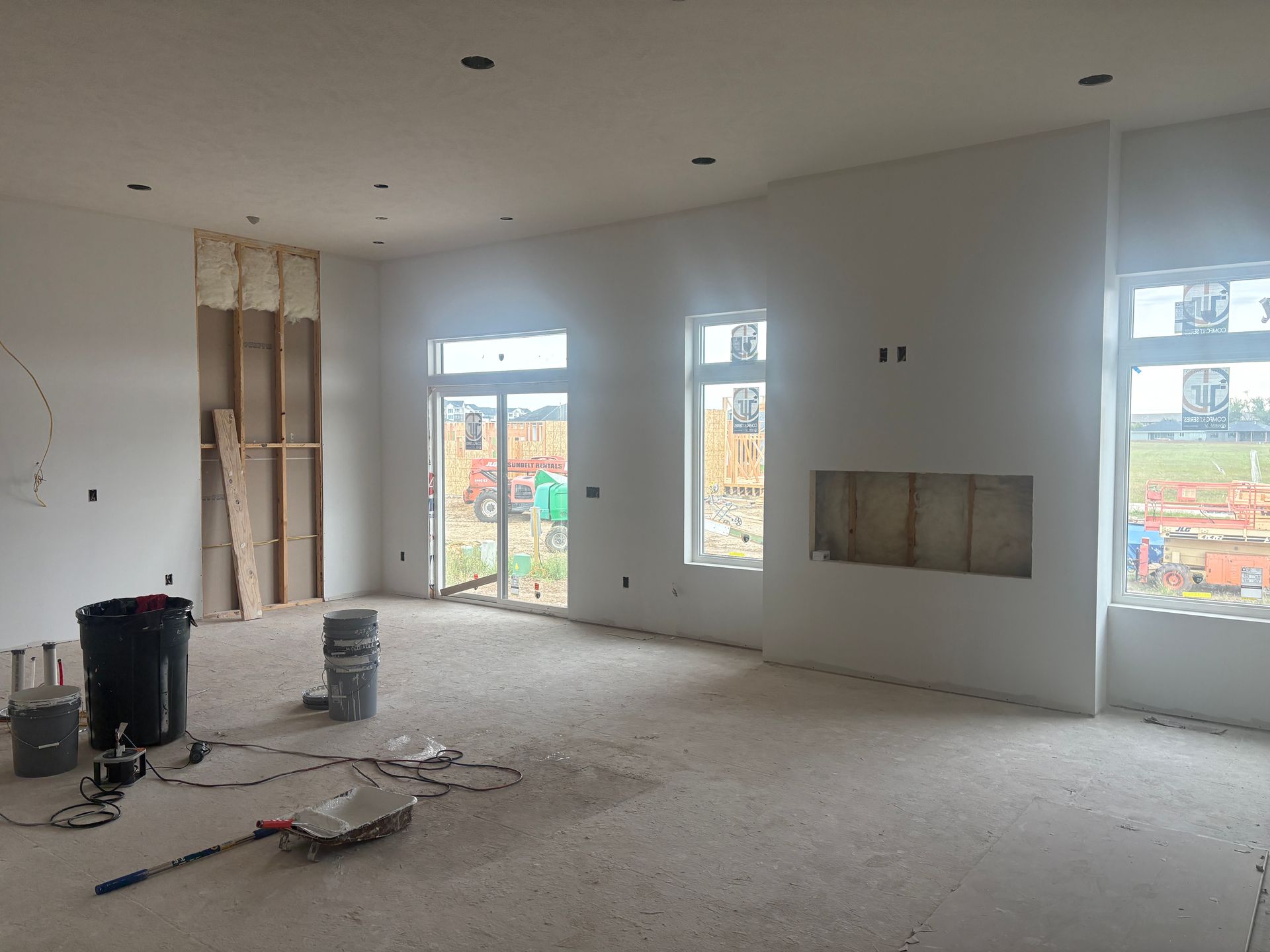 Interior of a room under construction, with white walls, windows, and exposed framing.