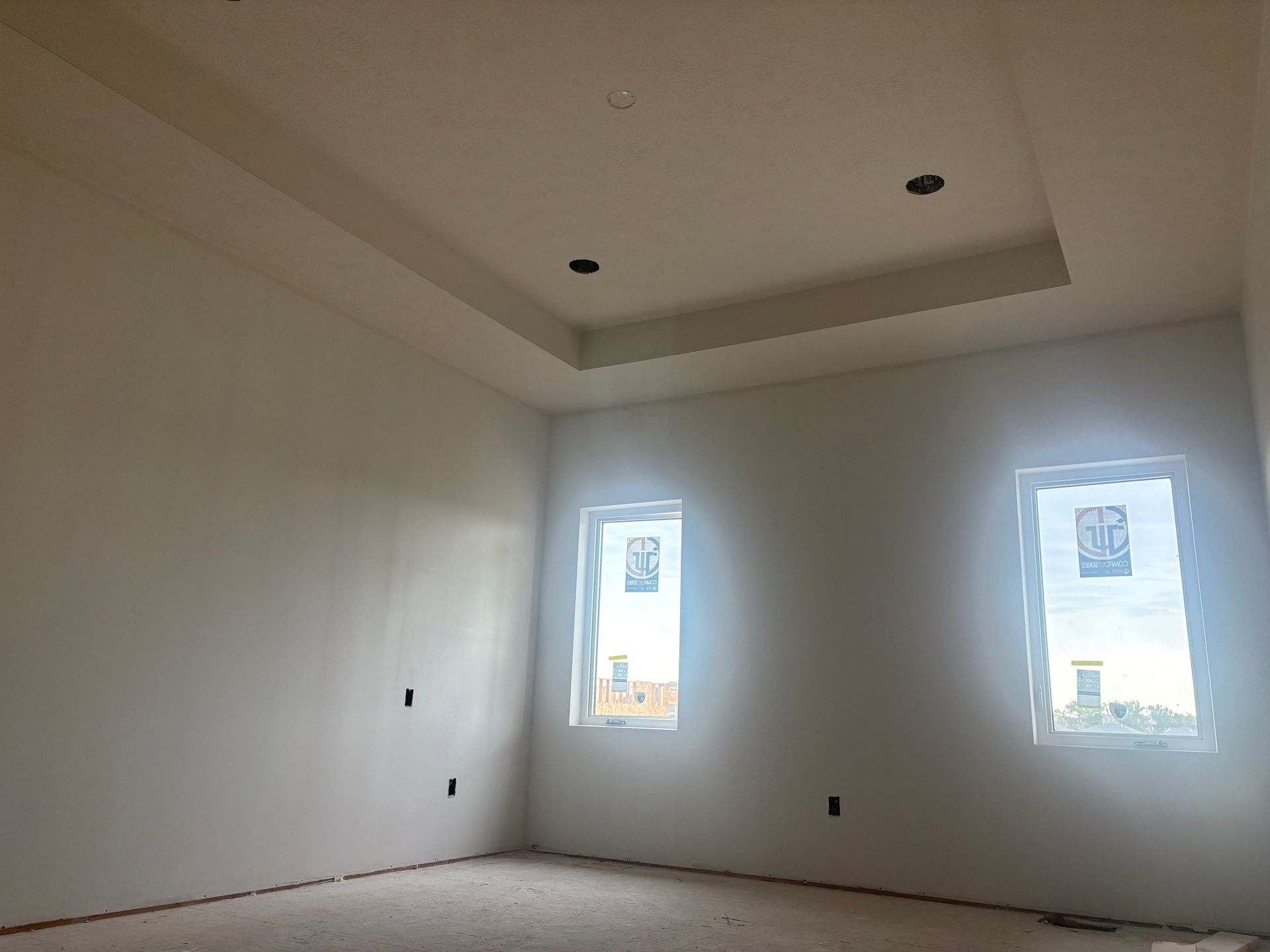 Empty room with white walls, two windows, and recessed ceiling lights.