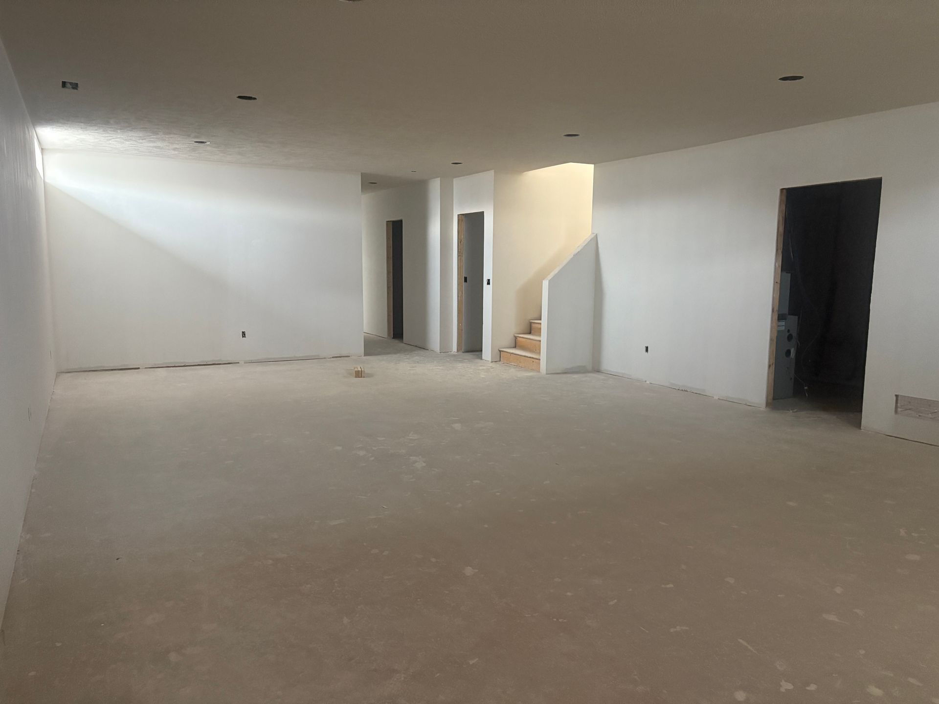 Empty room with unfinished walls, doors, and a staircase. Light-colored walls and floor.