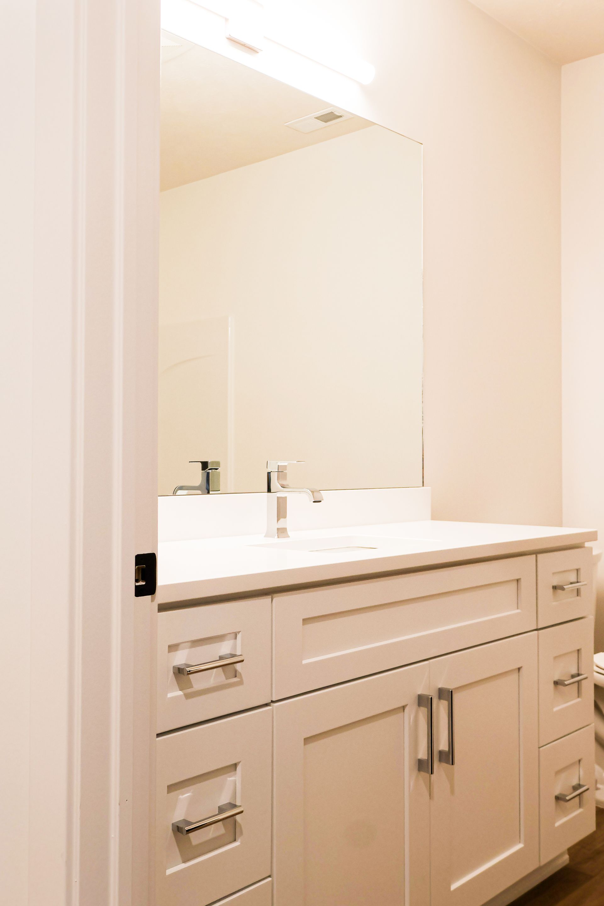 Bathroom vanity with white cabinet, white countertop, large mirror, and chrome fixtures.