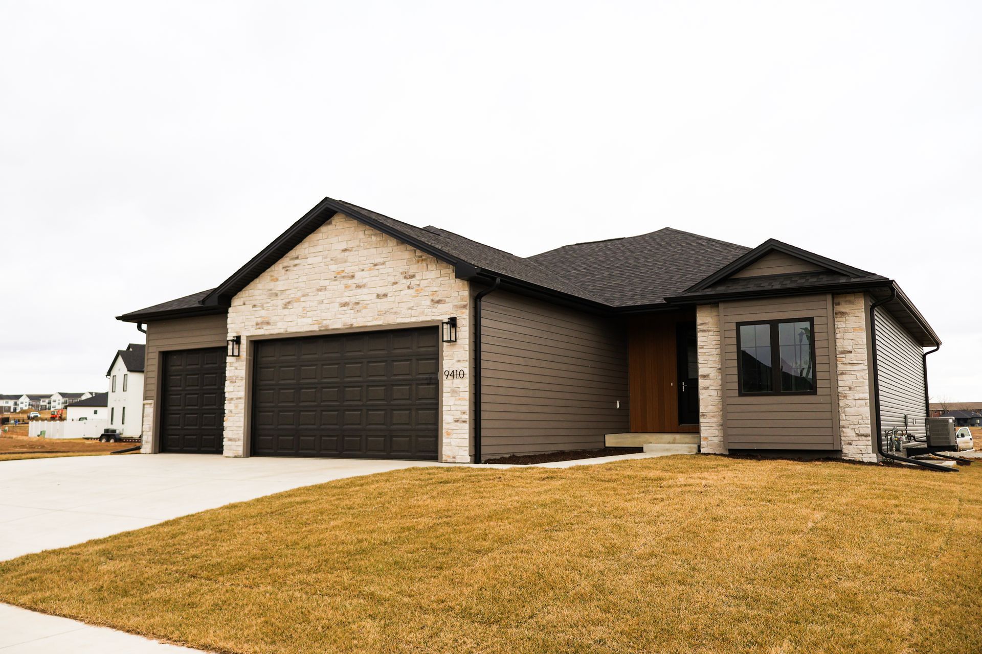 Modern house with gray and brick facade, two-car garage, and brown door on a cloudy day.